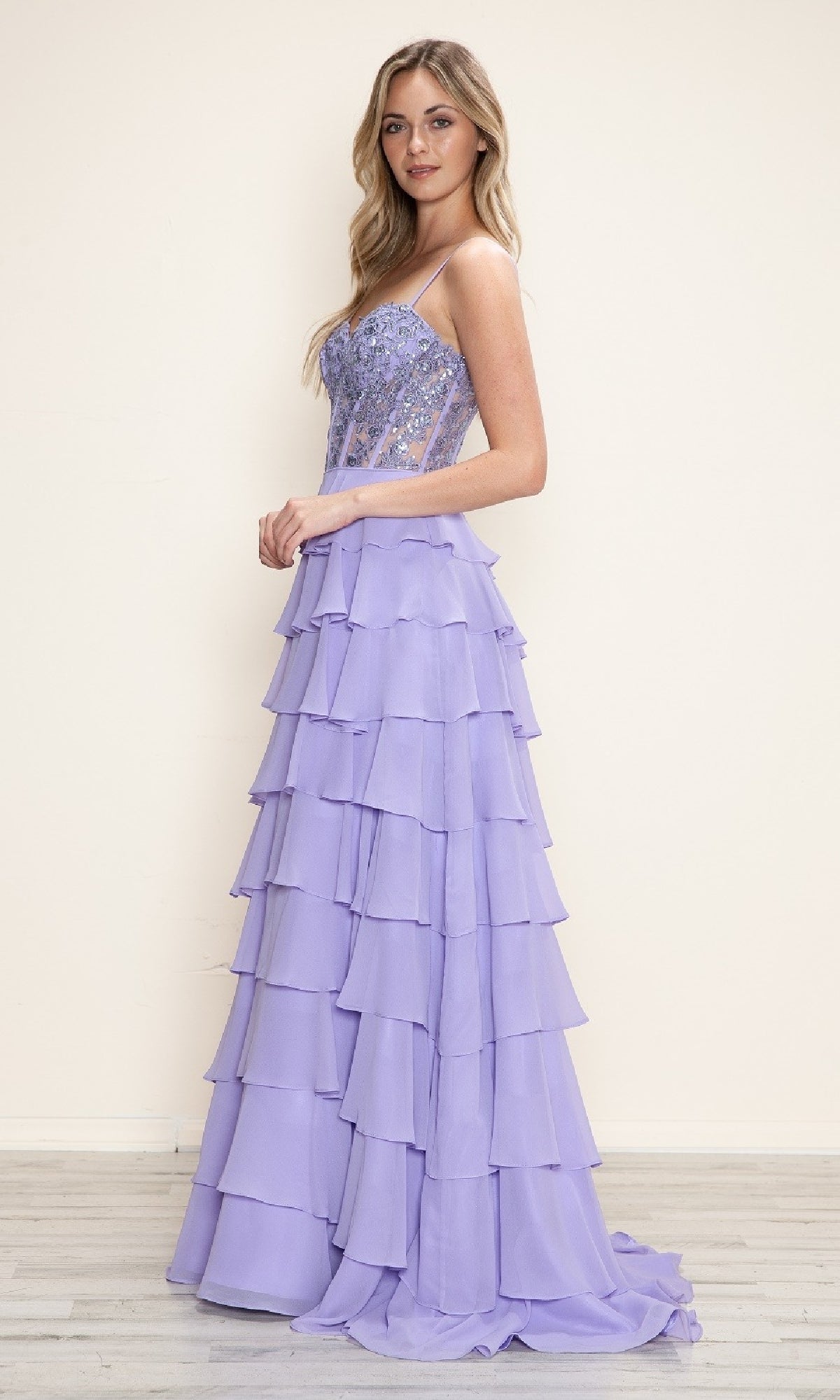 A woman stands sideways against a light background, wearing the Long Tiered Corset Prom Dress: Poly USA 9698 in lavender, featuring an A-line silhouette and corset-style bodice.