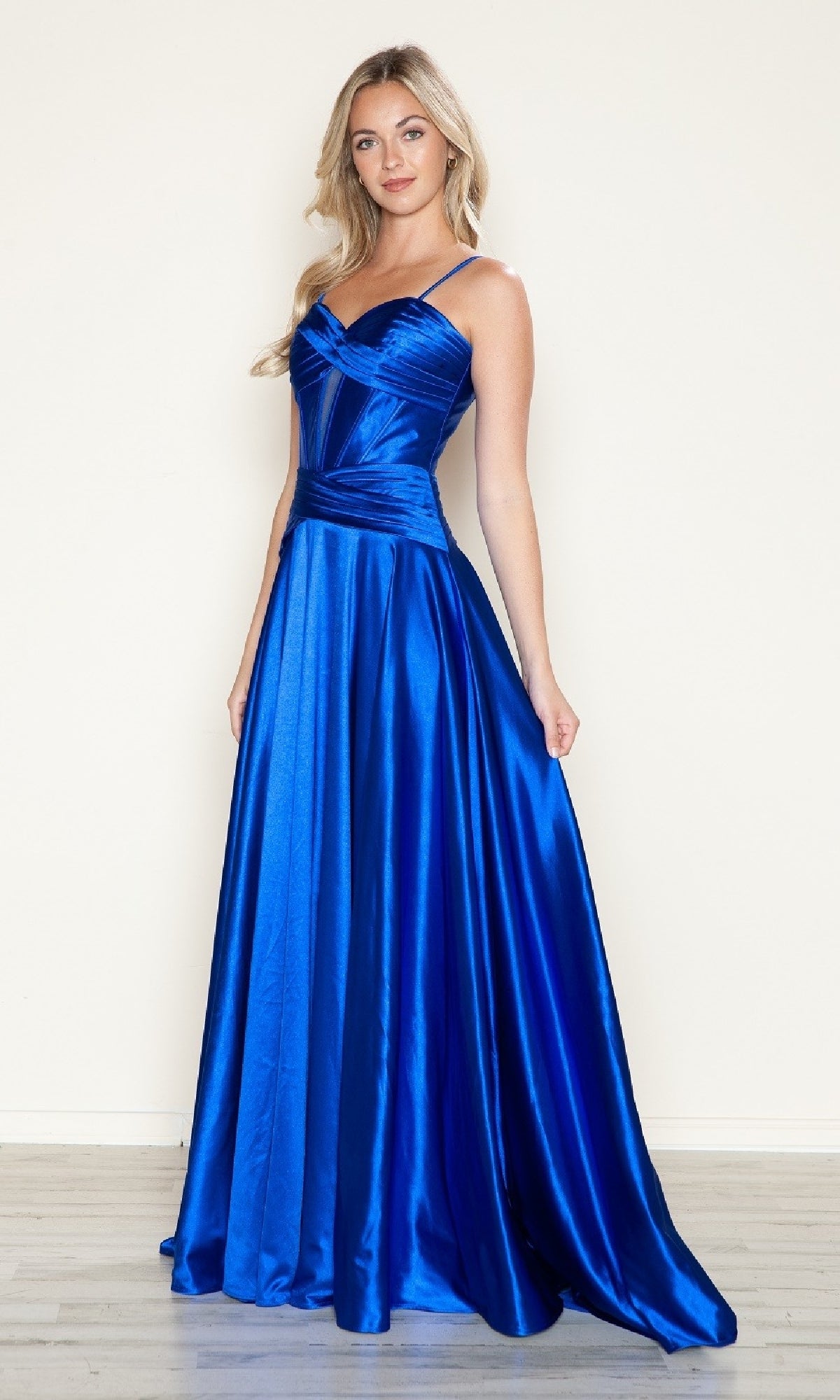 A woman wearing the Cut-Out Long A-Line Prom Dress: Poly USA 9700 in royal stands on a light wood floor against a plain cream wall.