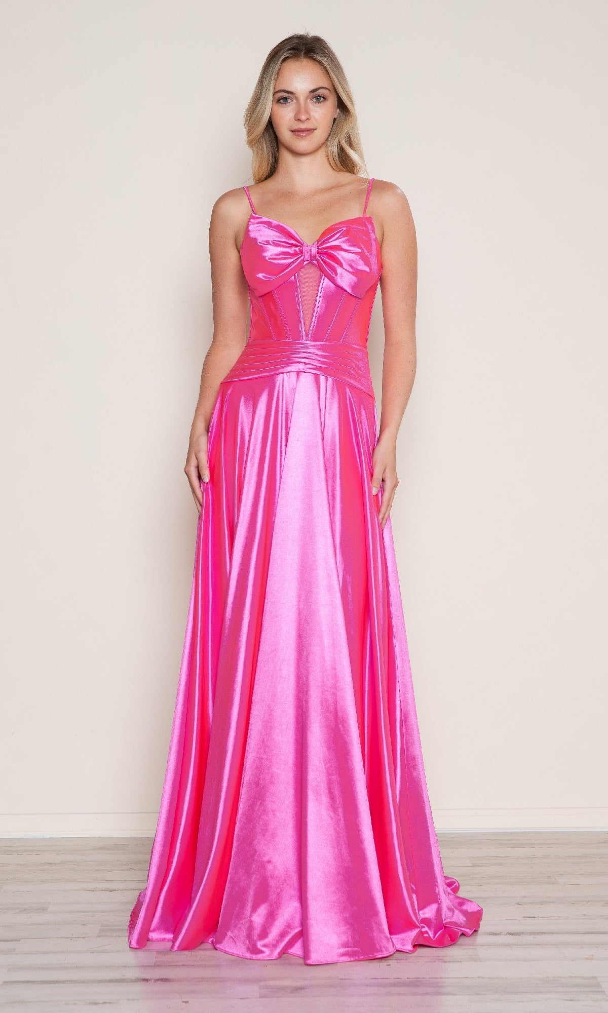 A woman faces forward wearing the Poly USA 9702 Bow-Front Long Corset Prom Dress in pink, featuring spaghetti straps, a floor-length silhouette, subtle cut-out corset details, and a bow-shaped bodice.