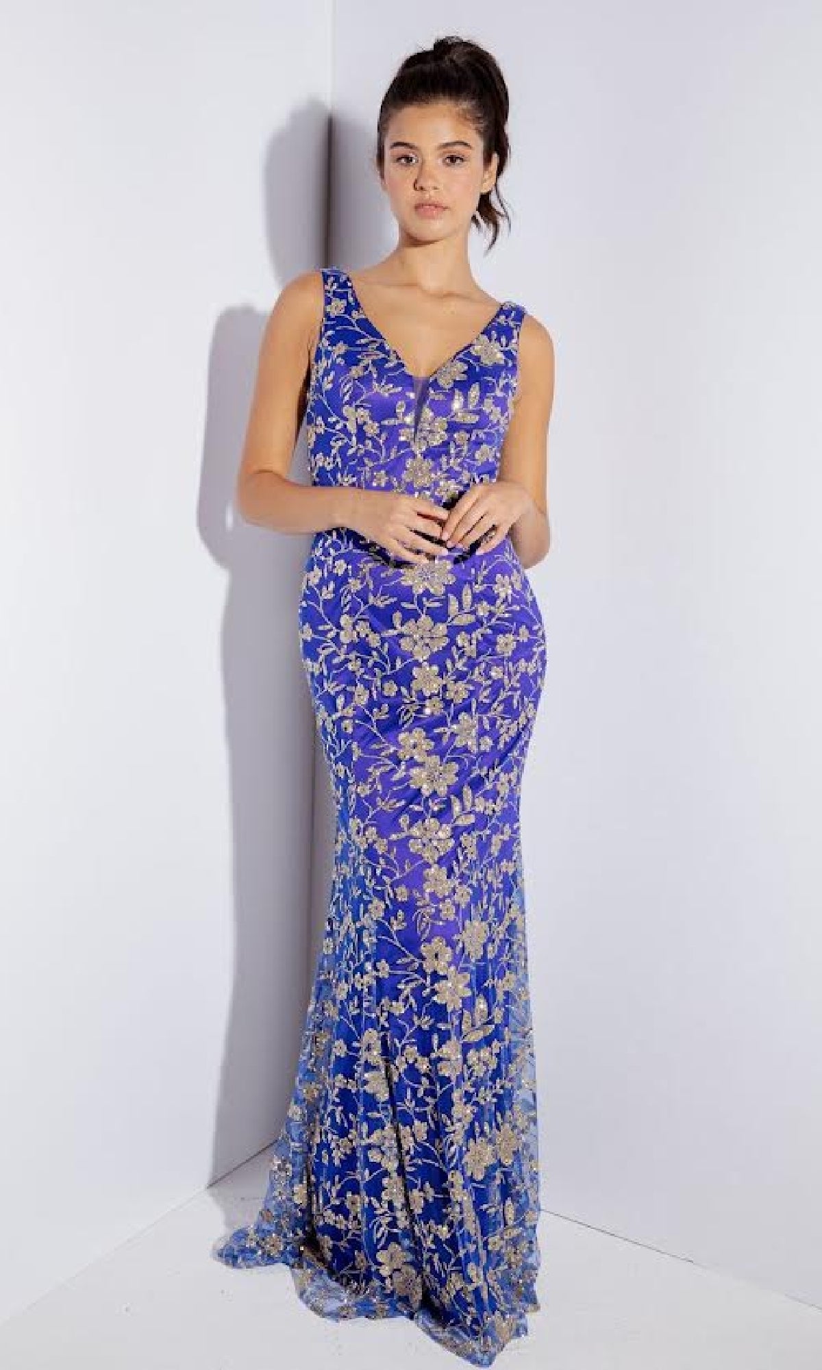 A woman stands against a white background wearing the Eureka 9706 Sequin-Print Long Prom Dress, a fitted, sleeveless royal blue gown with gold floral embroidery.