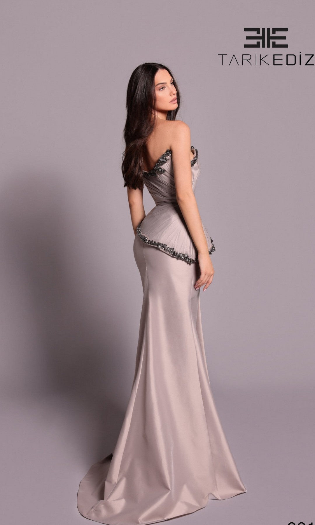 A woman poses against a plain background in the Tarik Ediz 99119 long formal dress, featuring a strapless taffeta design with a fitted silhouette and flared hem. The