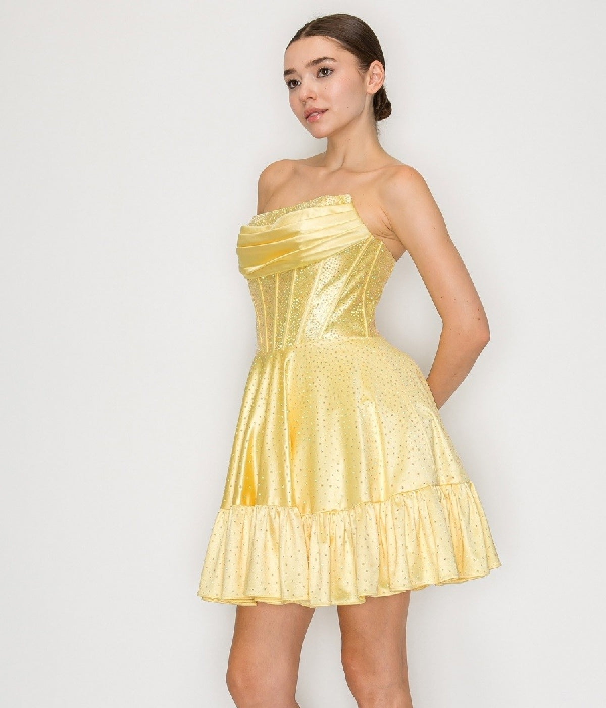 A woman models the Short Homecoming Dress: Poly USA 9942, featuring a strapless yellow fitted bodice and a ruffled hem, standing against a plain white background.
