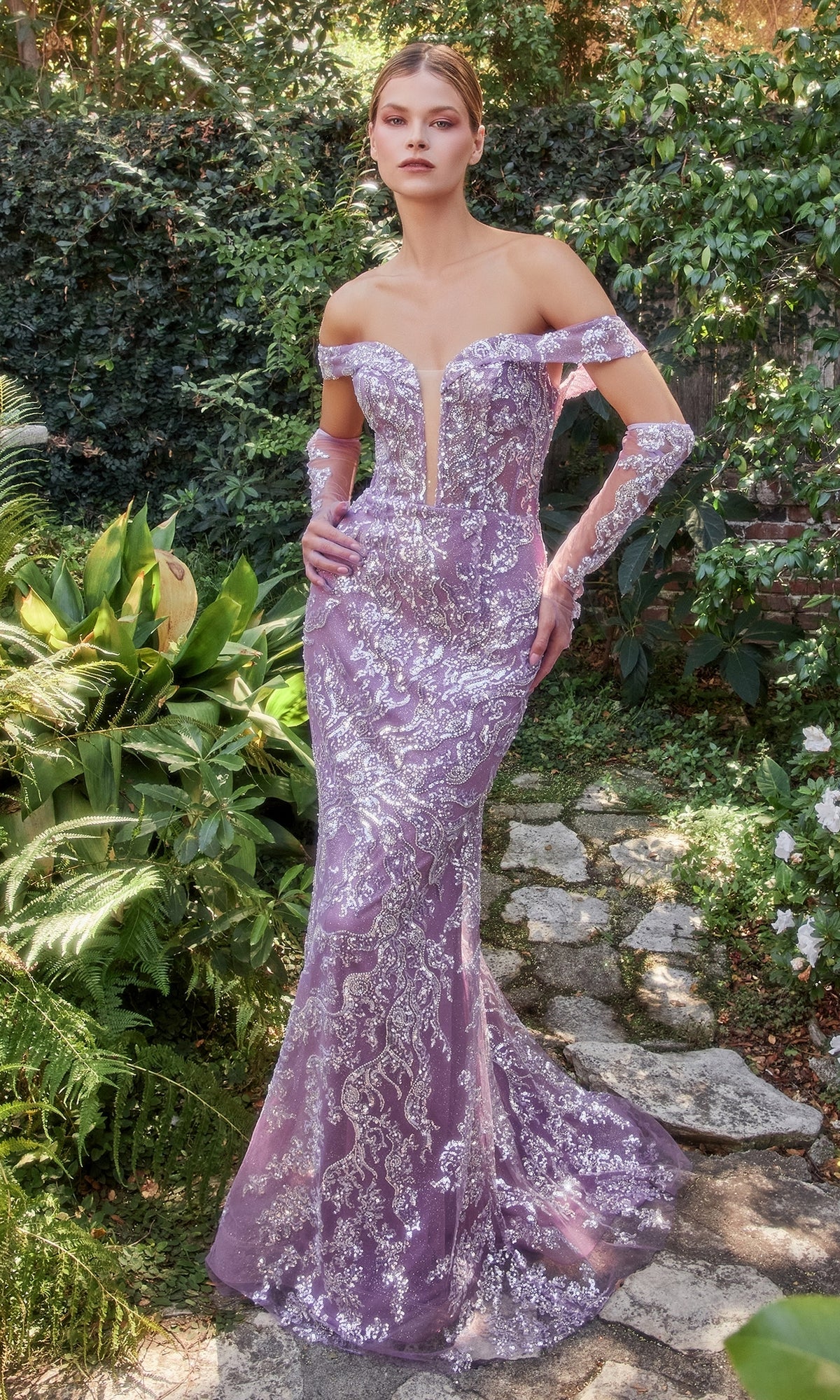 A woman stands on a stone path surrounded by greenery, wearing the Off-Shoulder Glitter Formal Dress with Gloves A1163 in lavender with silver embroidery.
