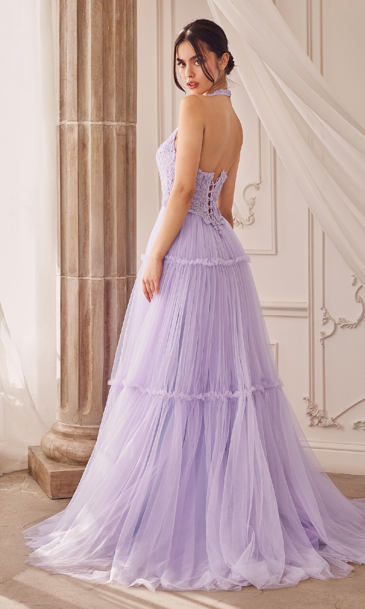 A woman stands indoors, looking over her shoulder in the Lace-Halter Long A-Line Prom Dress A1206, featuring a light purple hue with floral-lace bodice and halter neckline.