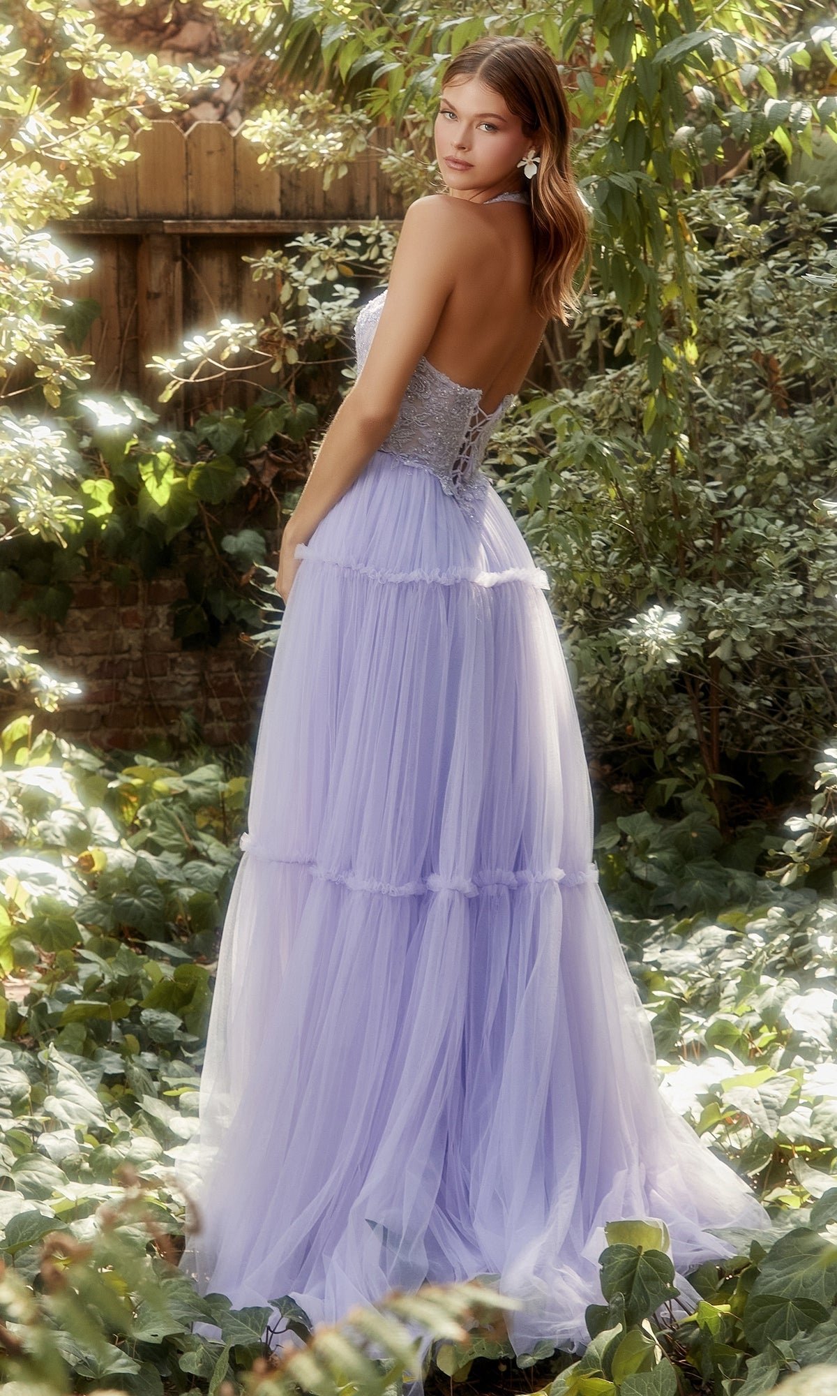 A woman in the Lace-Halter Long A-Line Prom Dress A1206 stands in a sunlit garden, looking over her shoulder toward the camera.