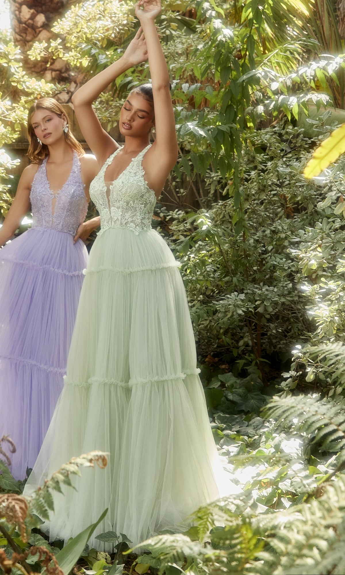 Two women wear Lace-Halter Long A-Line Prom Dress A1206—one in light green with a floral-lace bodice, one in lavender—standing in a sunlit garden surrounded by greenery.