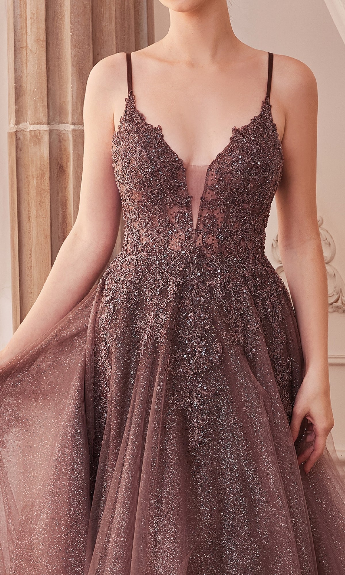 A woman wears the Sage Green Long Glitter-Tulle Prom Dress A1261, featuring a sleeveless, deep V-neck design with sequin details, and holds one side of the gown.