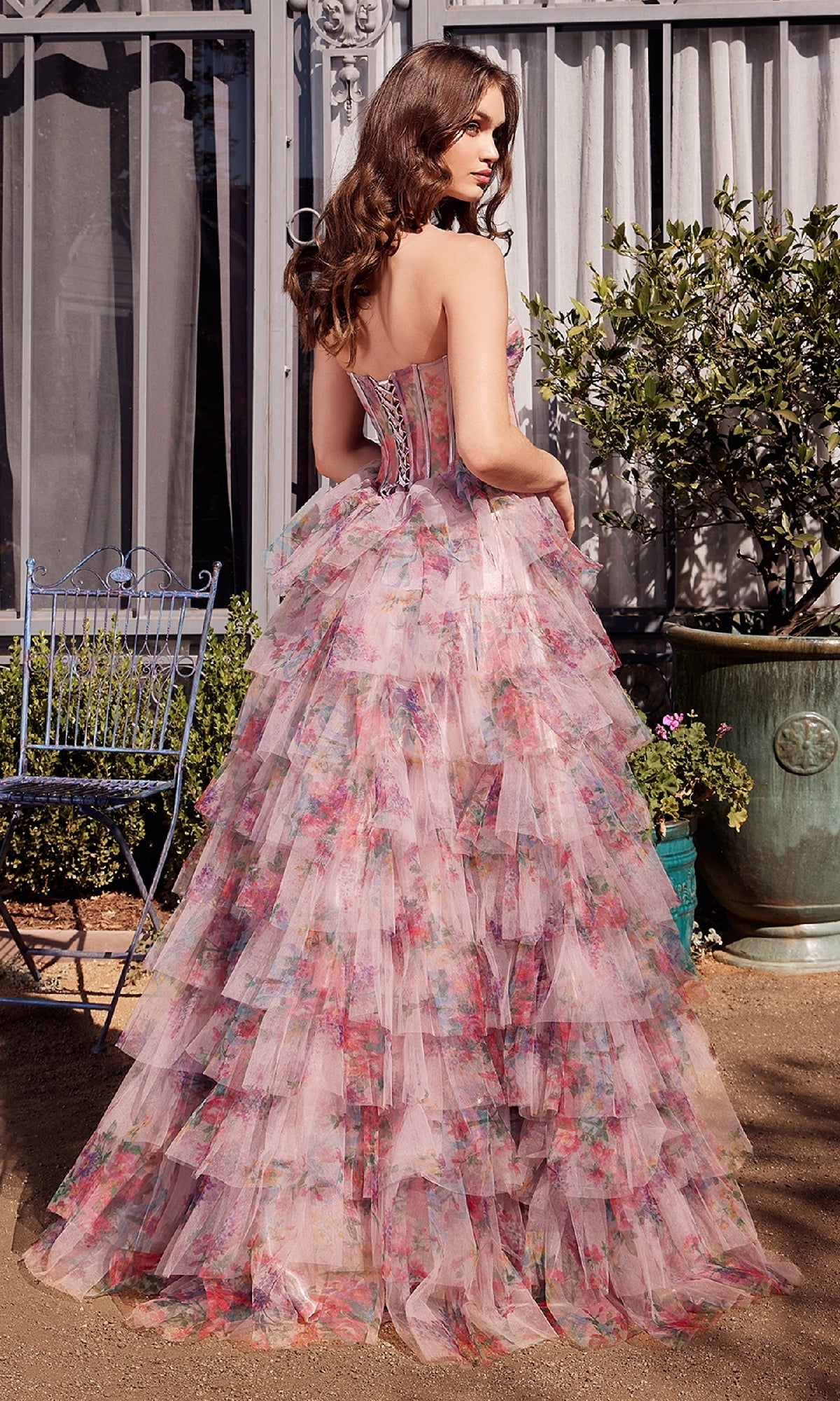 A woman stands outdoors facing away from the camera, wearing the Andrea & Leo A1463 Strapless Print Prom Ball Gown featuring layered ruffles and a floor-length skirt.