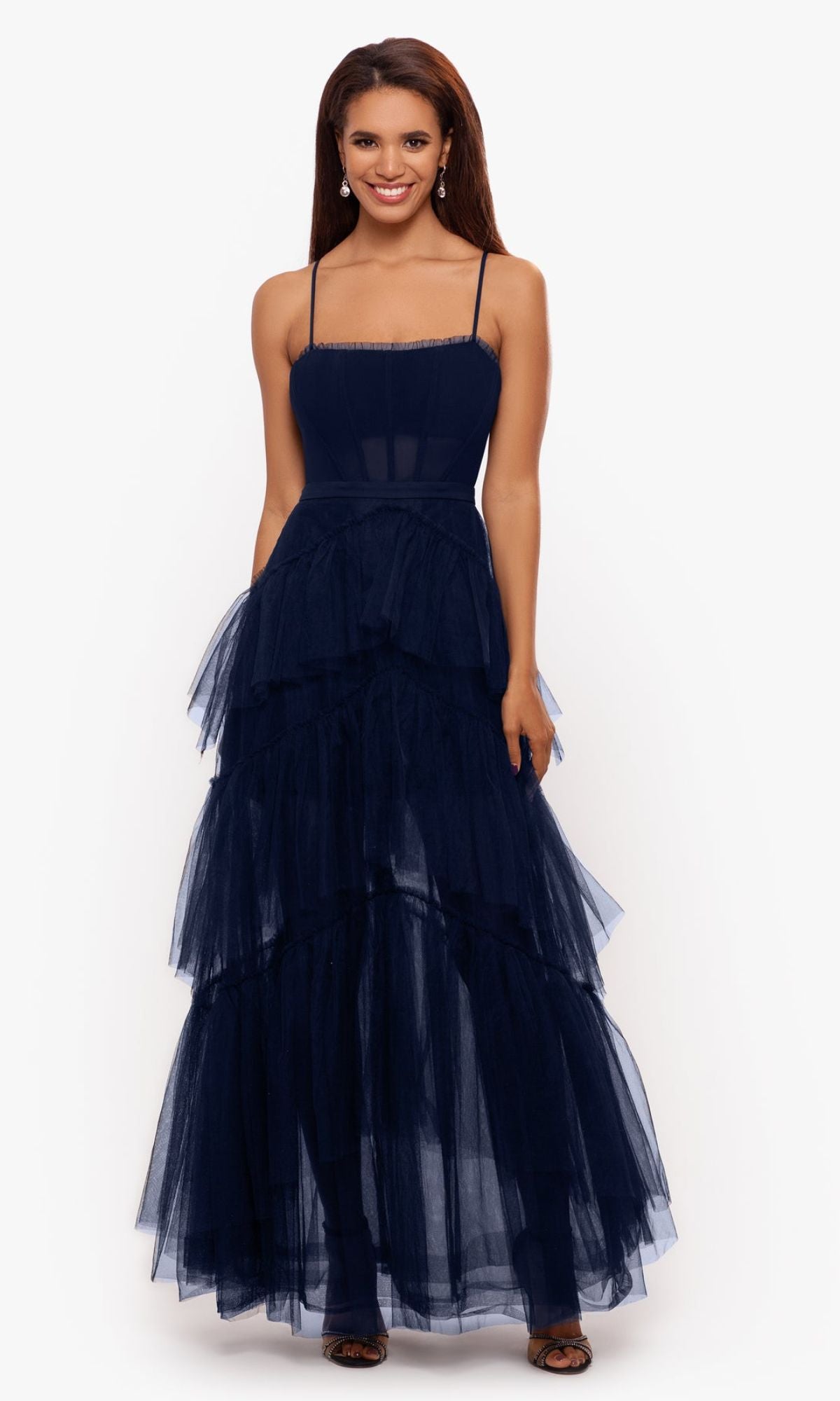 A woman smiles against a plain white background, wearing the Betsy and Adam Long Ruffled Prom Dress A24201—sleeveless, navy blue, and floor-length.