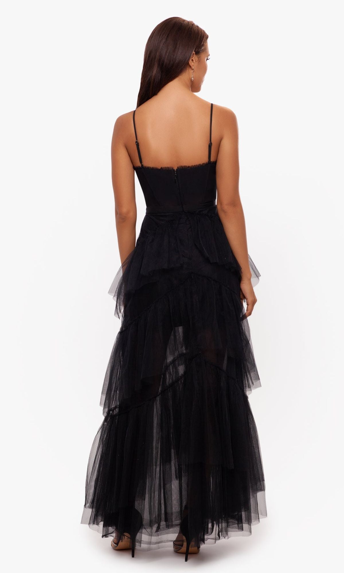 A woman is photographed from the back against a white background wearing the Betsy and Adam Long Ruffled Prom Dress A24201—a black tiered tulle evening gown with spaghetti straps.