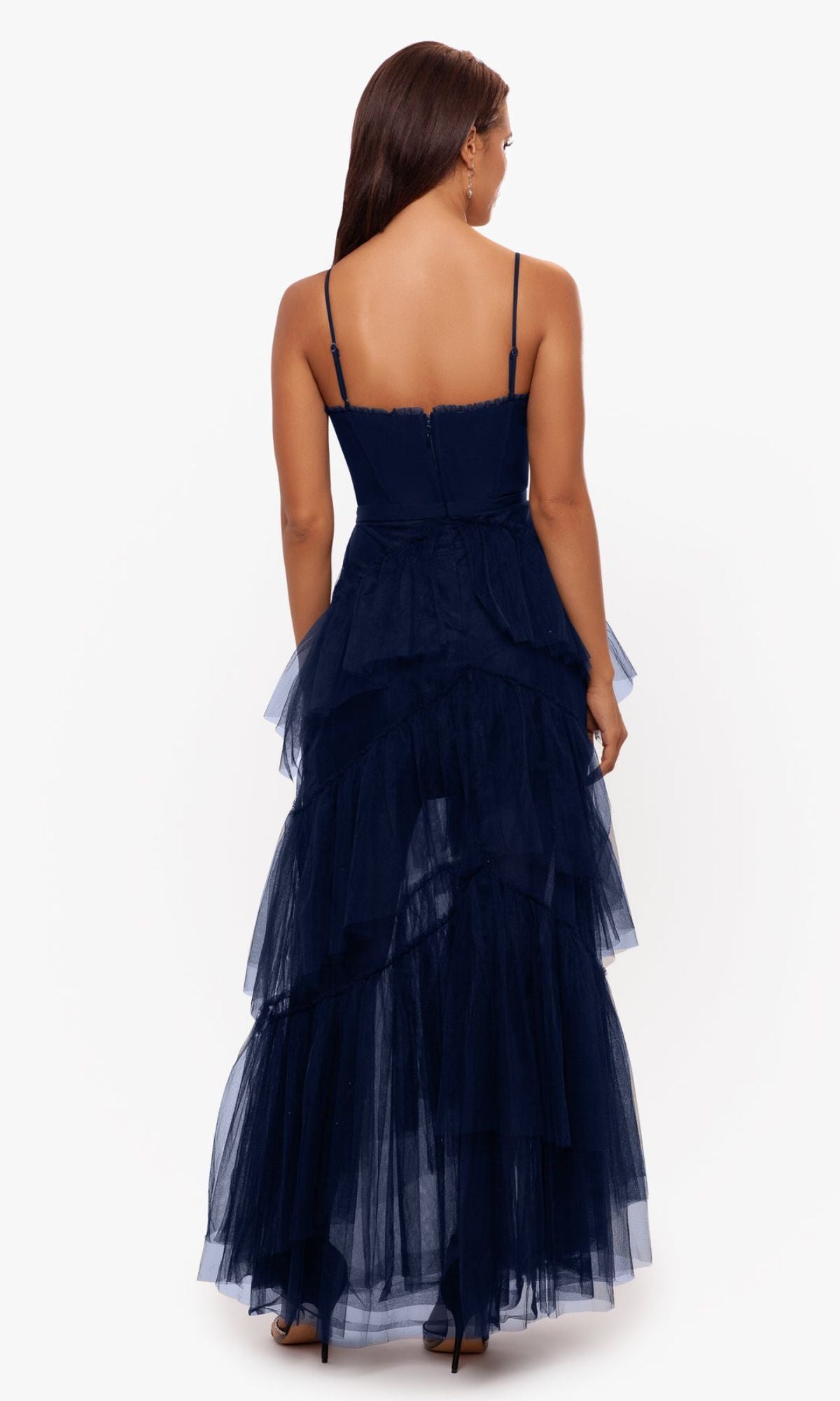 A woman is shown from the back wearing the Betsy and Adam Long Ruffled Prom Dress A24201 in navy blue, featuring spaghetti straps and tiered tulle layers, against a plain white background.