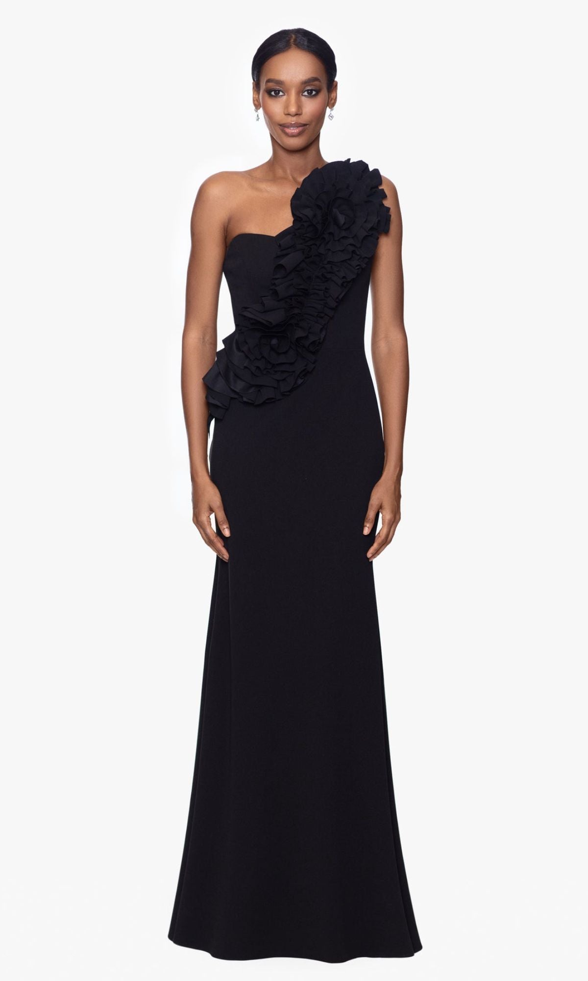 A woman faces forward in the Betsy and Adam One-Shoulder Long Prom Dress A26071, a black evening gown featuring ruffle details across the front and shoulder, set against a plain white background.