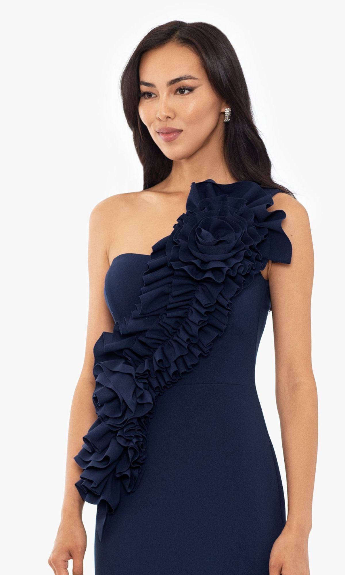 Woman wearing the Betsy and Adam One-Shoulder Long Prom Dress A26071 in navy blue, featuring a dramatic ruffled floral detail across the front, posed against a plain white background.