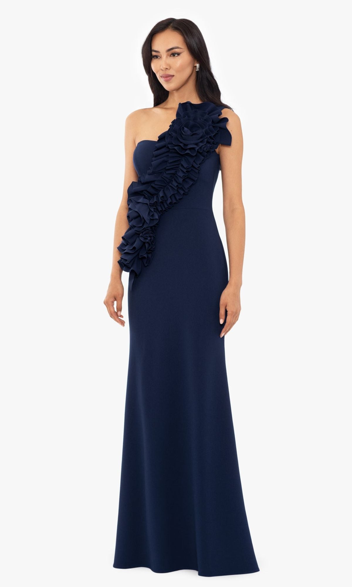 A woman wears the Betsy and Adam One-Shoulder Long Prom Dress A26071 in navy blue, featuring a large front ruffle, posing against a plain white background.
