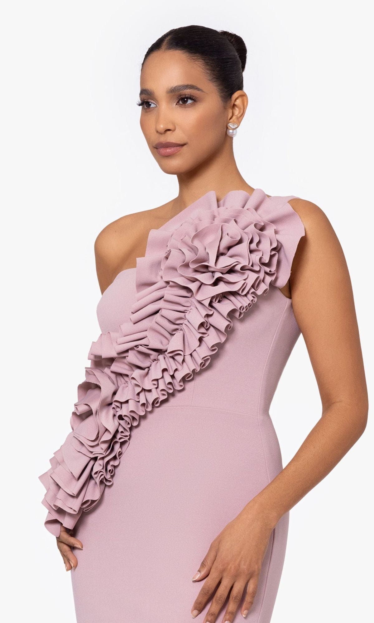 A woman models the Betsy and Adam One-Shoulder Long Prom Dress A26071 in mauve, featuring a large ruffle detail across the front, against a plain light background.