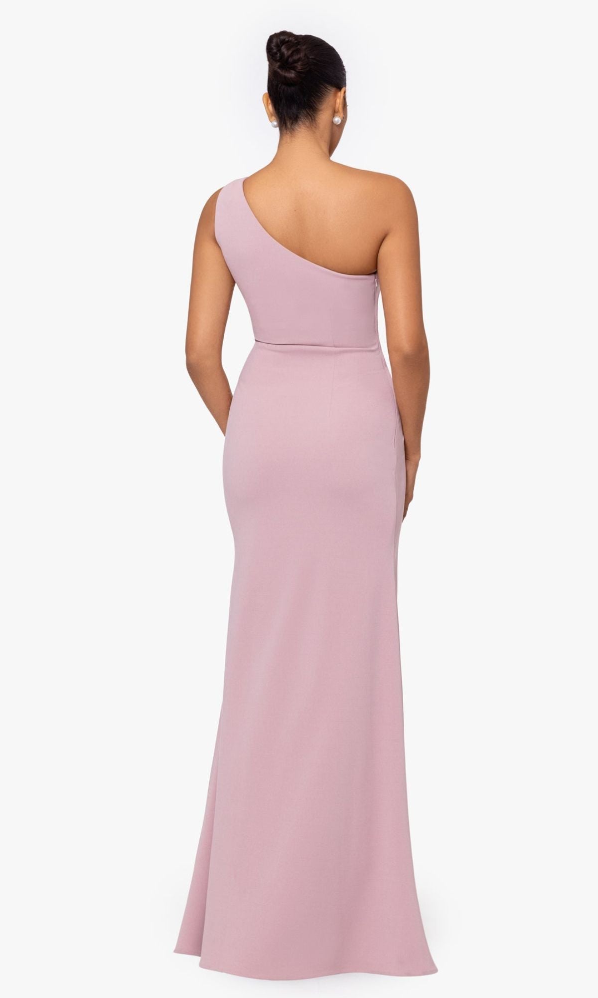 A woman stands with her back to the camera, modeling the Betsy and Adam One-Shoulder Long Prom Dress A26071 in light mauve against a plain white background.