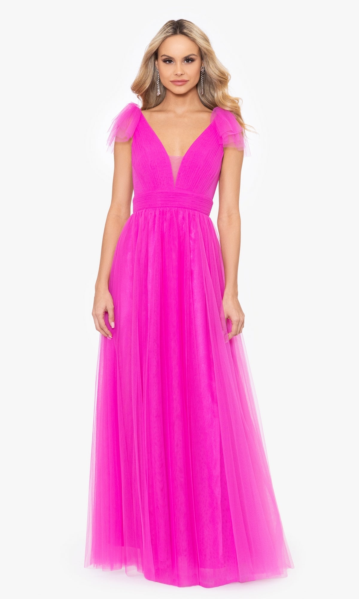 A woman models the Betsy & Adam Shoulder-Bow Long Prom Dress A26256, featuring bright pink tulle, a floor-length A-line silhouette, deep V-neckline, and cap sleeves, standing against a plain white background.