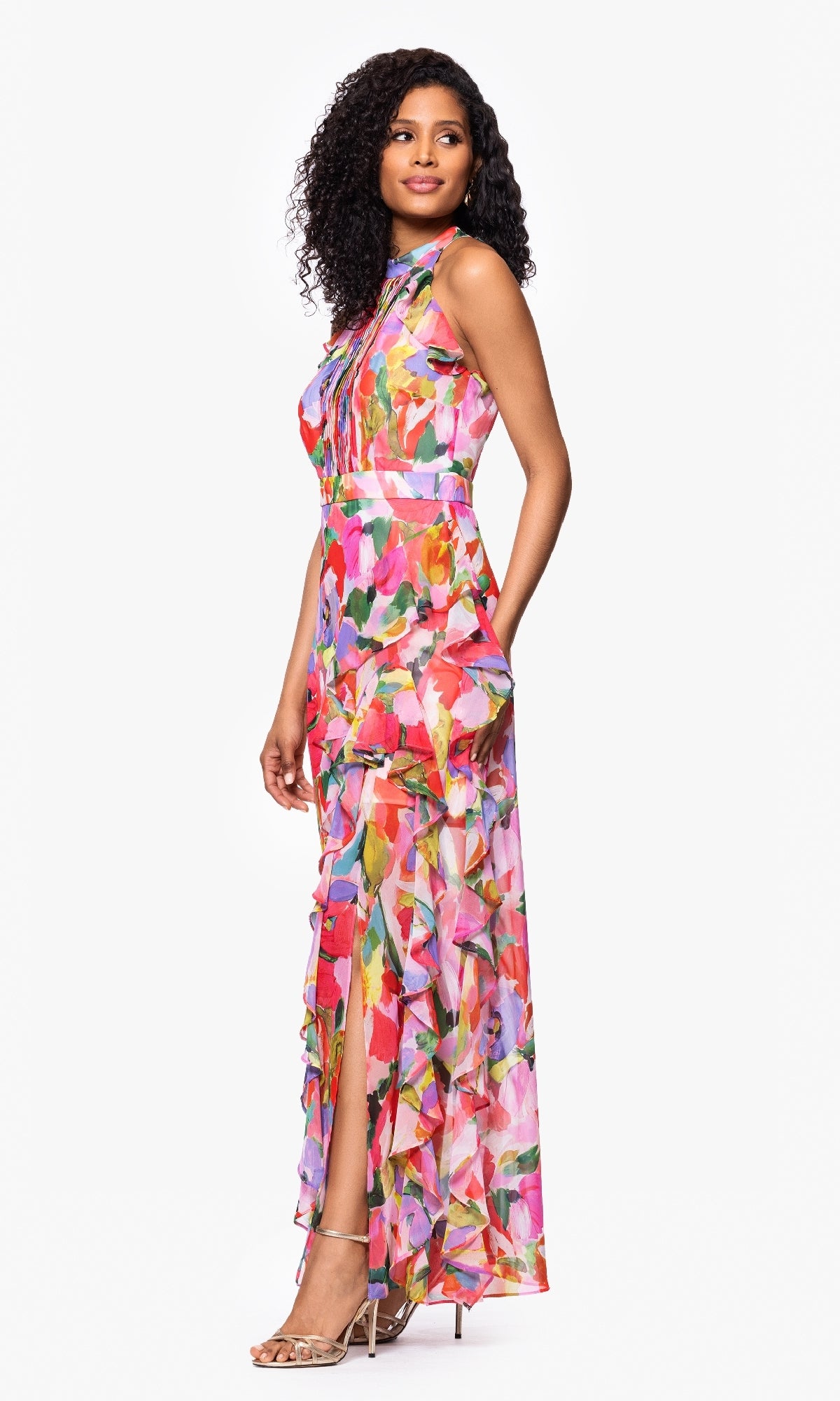 Woman in the Betsy & Adam A27022 Floral Wedding Guest Dress with a sleeveless watercolor print, high neckline, side slit, and nude heeled sandals stands against a white background—an elegant choice for formal wedding guests.