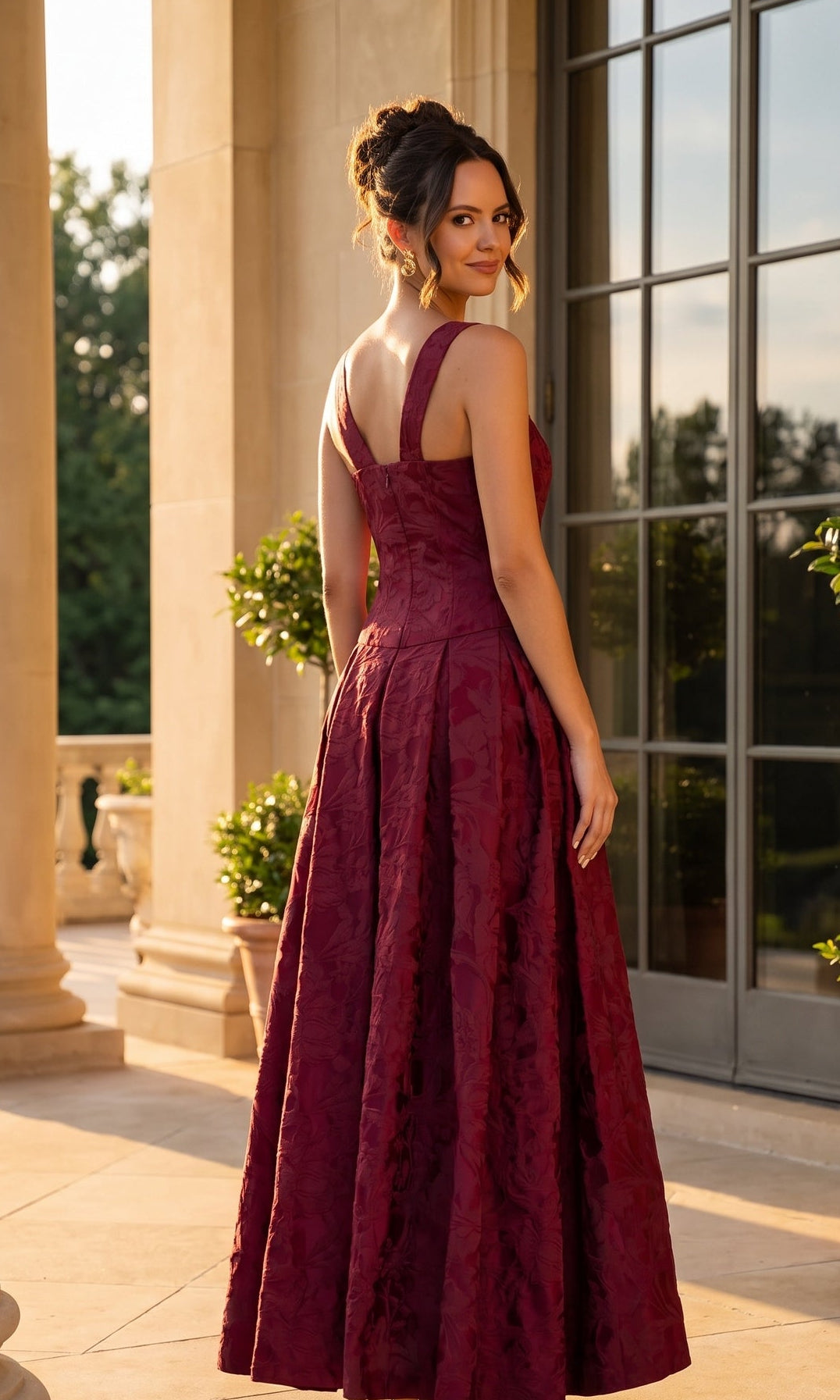 A woman wearing the Betsy & Adam A28250 long formal dress stands outside by a glass door, turning slightly to look over her shoulder in the sunlight.