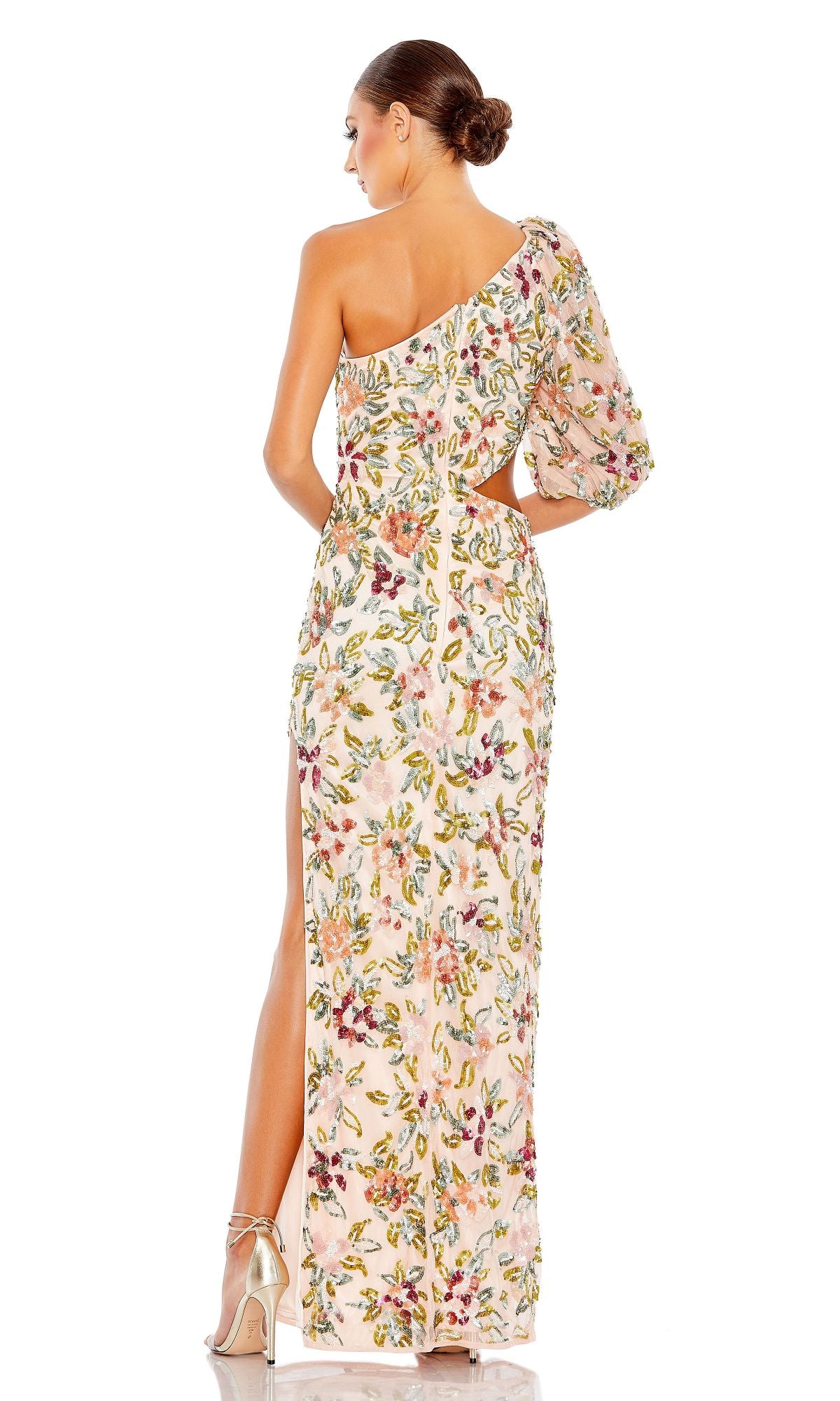 A woman faces away, wearing the Mac Duggal A5567 Floral-Sequin Long Formal Dress with a one-shoulder design, side slit, and nude heels. Her hair is styled in a low bun.