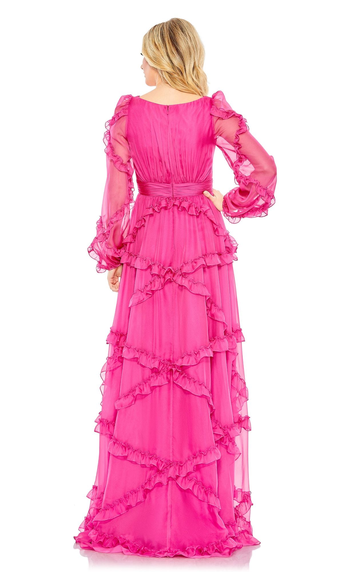 A woman faces away, wearing the Mac Duggal A68223 Long Sleeve Long Formal Dress in bright pink, featuring sheer sleeves and layered ruffle details.