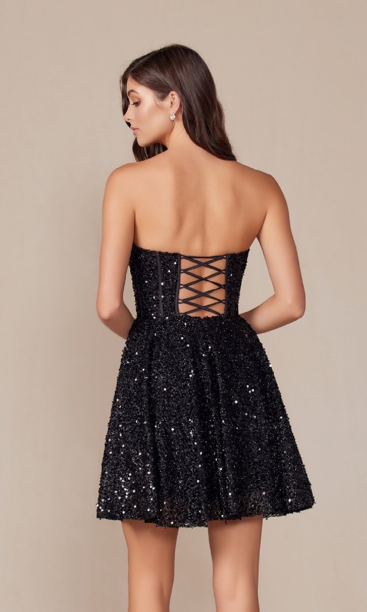 Woman in the Sequin Corset Homecoming Dress: Nox Anabel A843, featuring a strapless fit-and-flare silhouette with sequins and a crisscross lace-up back, standing against a plain background.