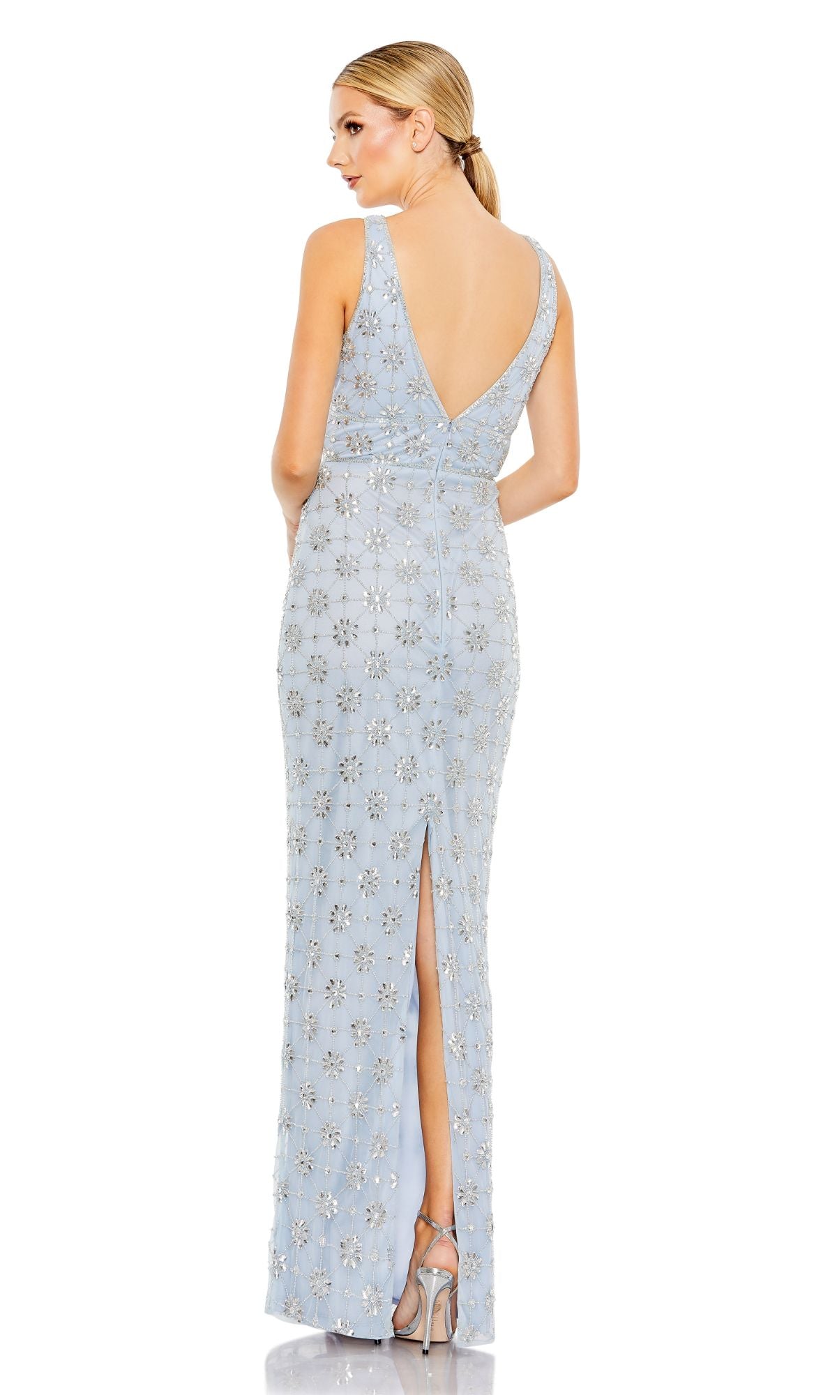 Woman wearing the Mac Duggal 93744 V-Neck Long Beaded Formal Dress, a floor-length, sleeveless gown in light blue with silver floral embellishments, deep V-back, and back slit, styled with high-heeled sandals.
