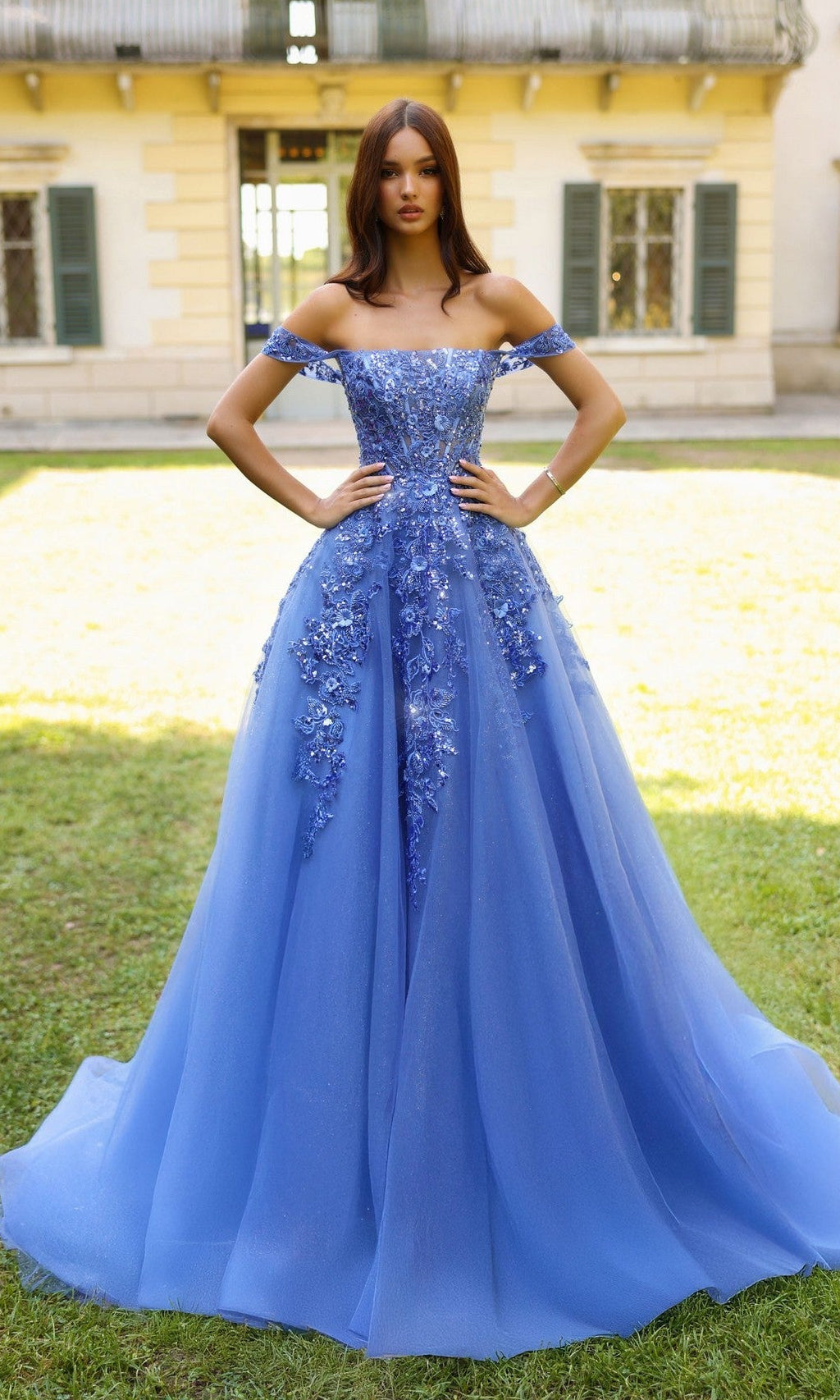Woman in a blue evening gown standing in front of a building with green grass.