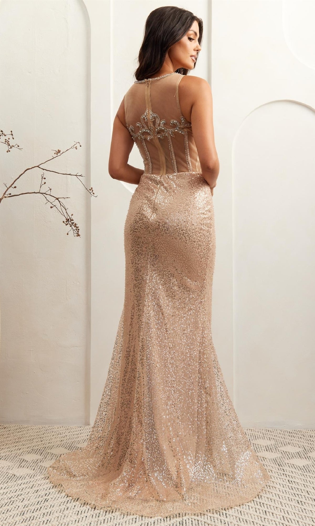Woman modeling the back of a sparkly gold evening gown with a plain background