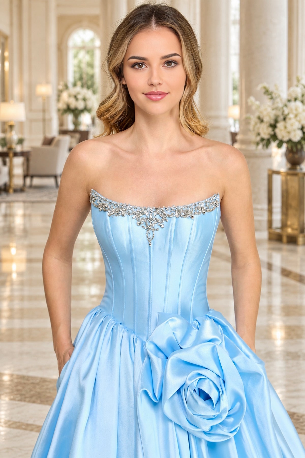 A woman wears a light blue Corset Prom Ball Gown: Amelia Couture AL1401, featuring a strapless, crystal-embellished neckline and a large fabric flower accent at the waist.