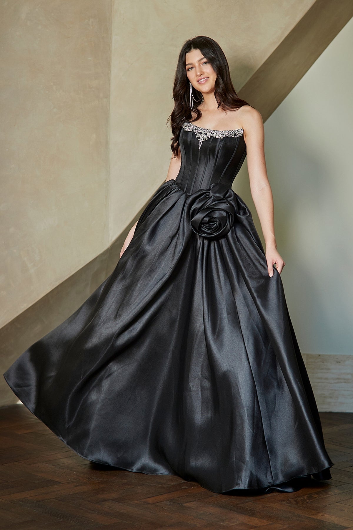Amelia Couture AL1401 strapless black ball gown featuring a corset bodice with jeweled neckline detailing and a large fabric flower accent at the waist.