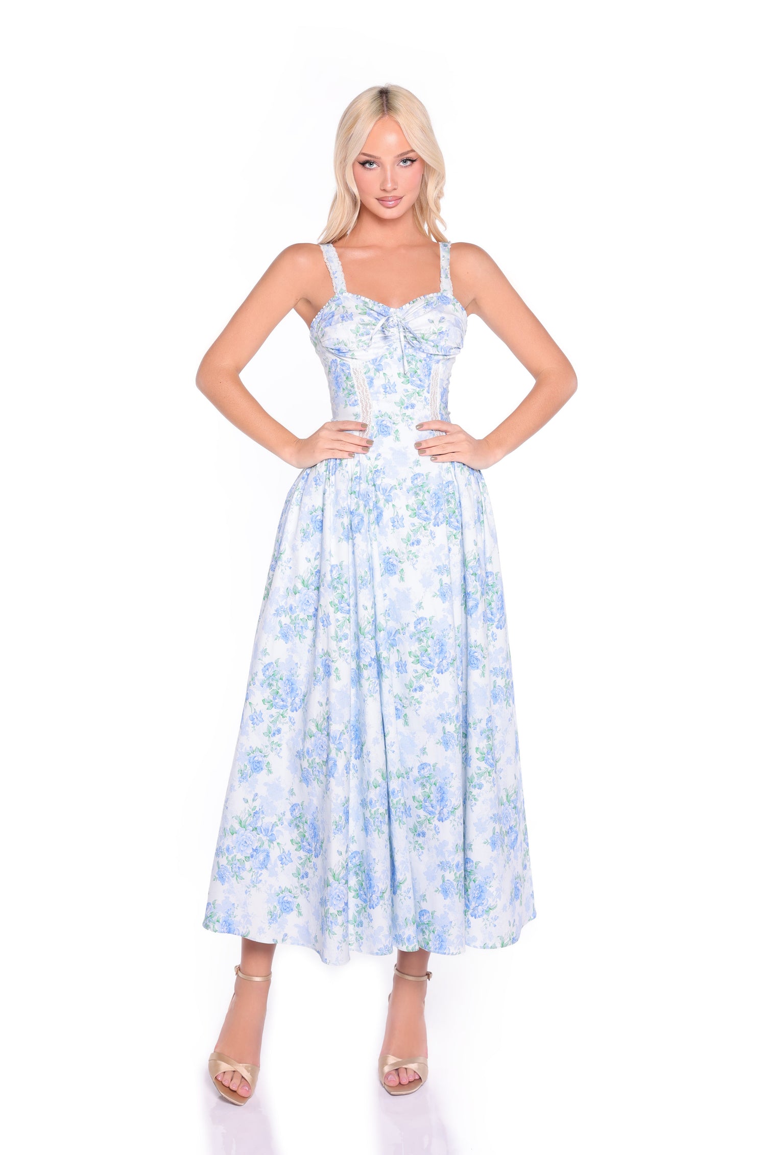 A woman stands with hands on hips, wearing the Anselma Blue Floral Cotton Summer Midi Dress and nude heels against a white background—perfect for summer weddings.