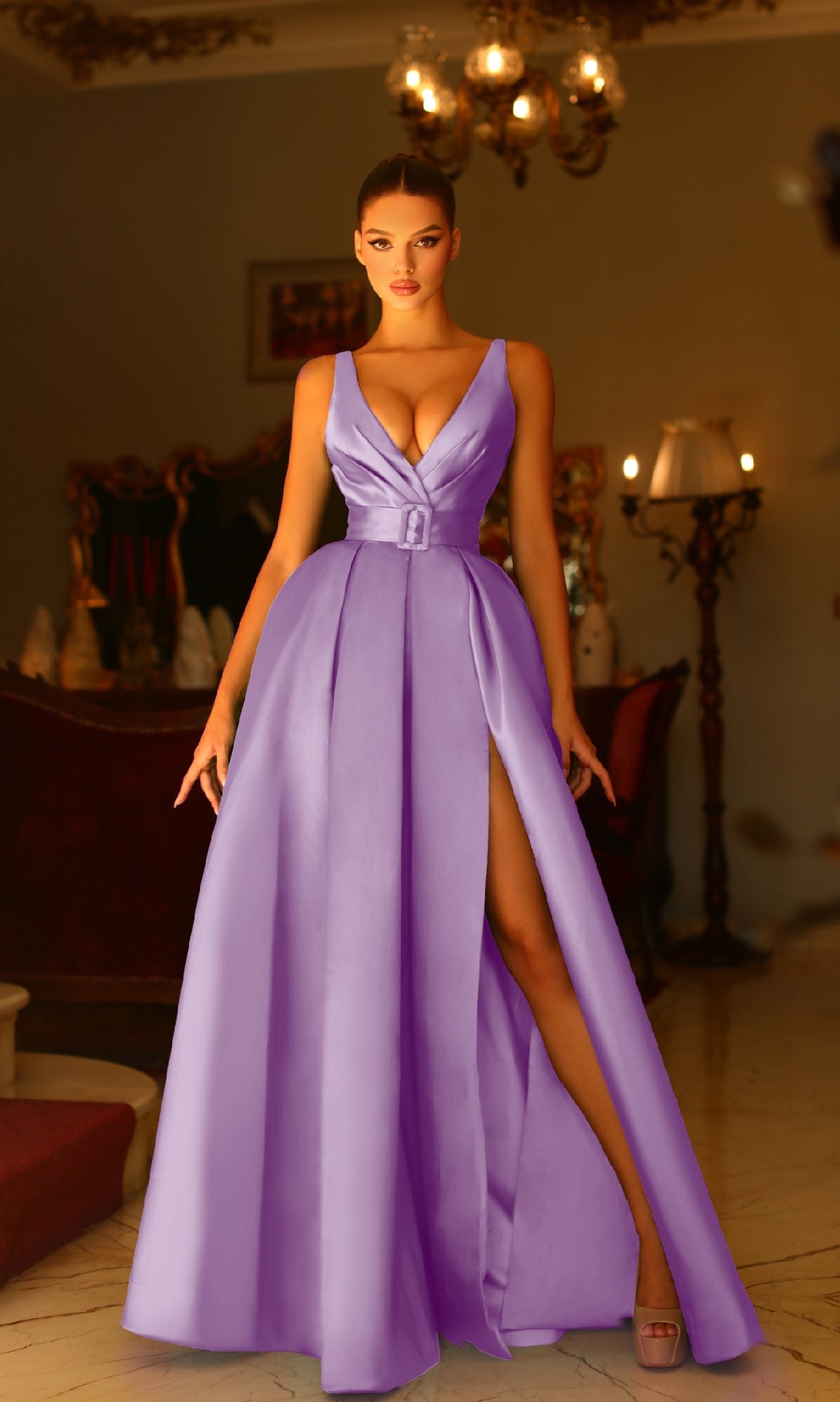 A woman stands indoors wearing the Tina Holly BB209 belted long prom ball gown, a sleeveless lavender A-line dress with a deep V-neckline and high slit, in an elegantly decorated room with warm lighting.
