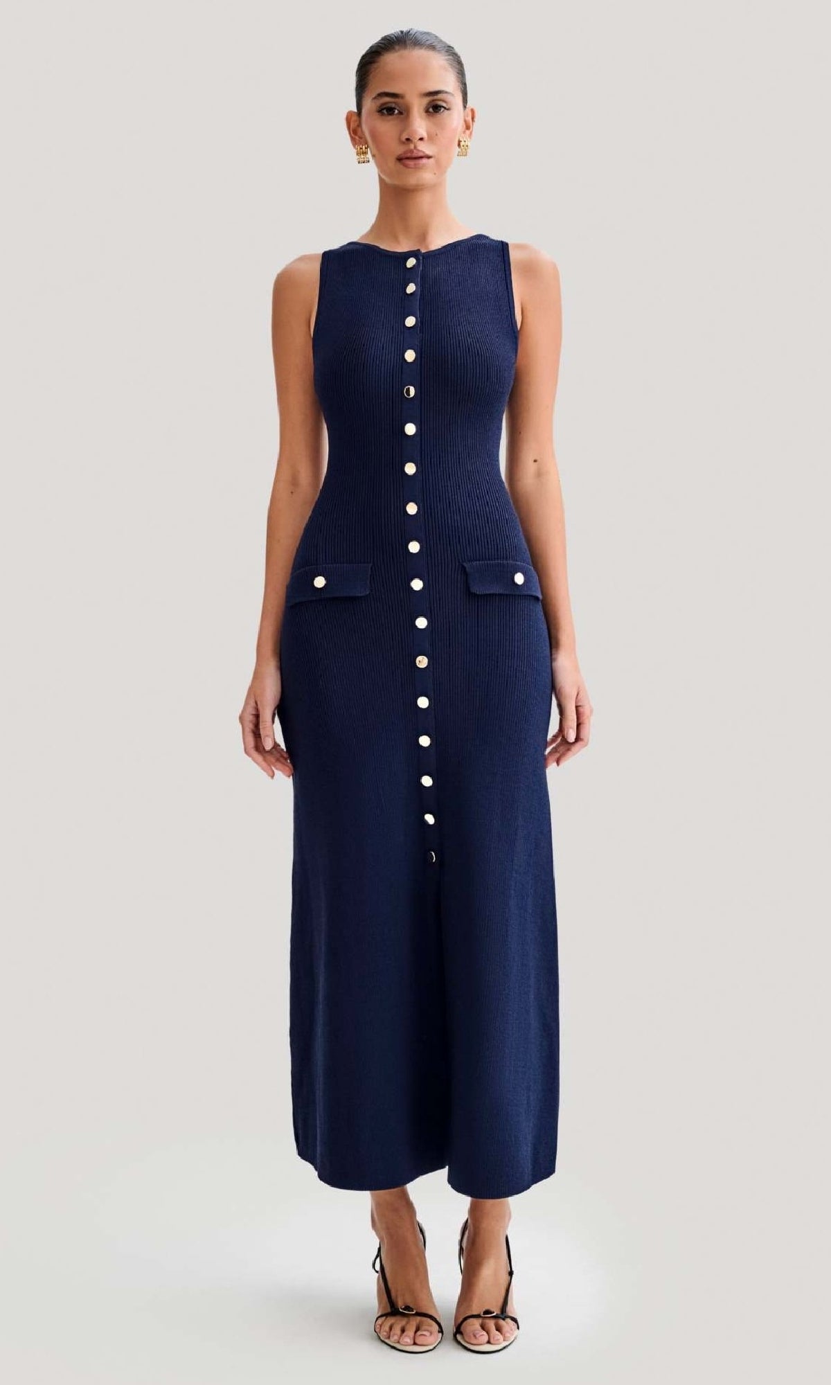 A woman faces forward wearing the Sleeveless Casual Button-Down Maxi Dress in navy blue with front buttons, two flap pockets, and black heeled sandals.