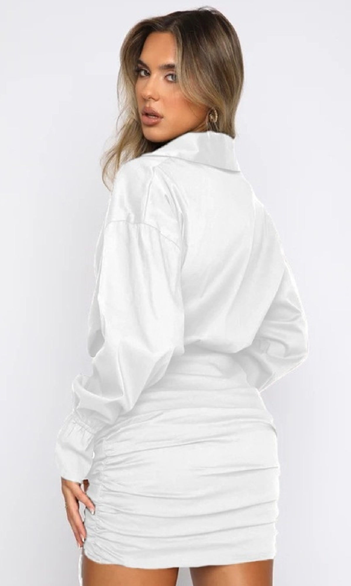 A woman in a Short Casual Shirt Dress with Long Sleeves, white and collared, stands with her back to the camera and looks over her shoulder against a plain background—a timeless casual style.