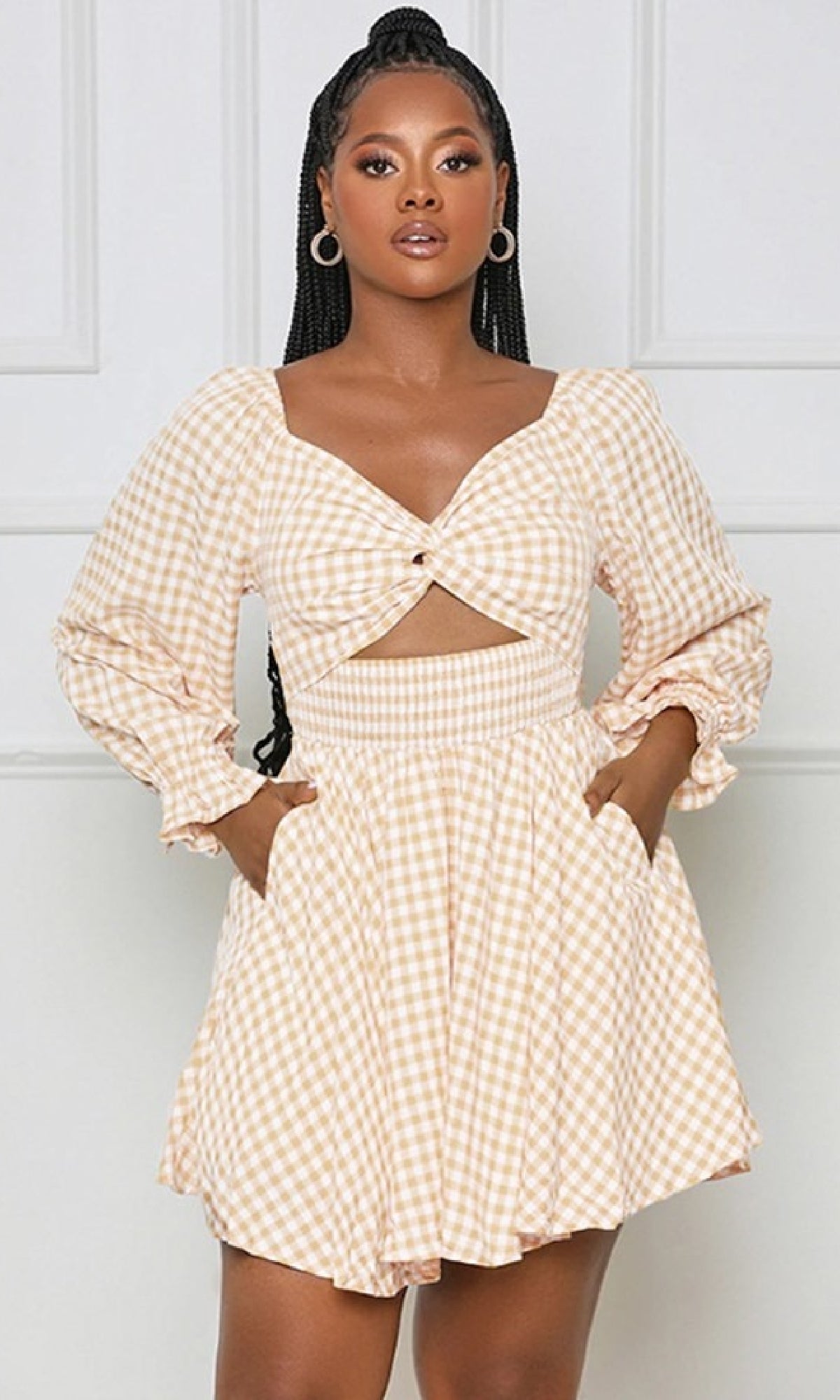 A woman stands against a plain light background wearing the Long-Sleeve Short Casual Gingham Print Dress in apricot, featuring an a-line silhouette, long sleeves, front cut-out, pockets, and a light gingham print.