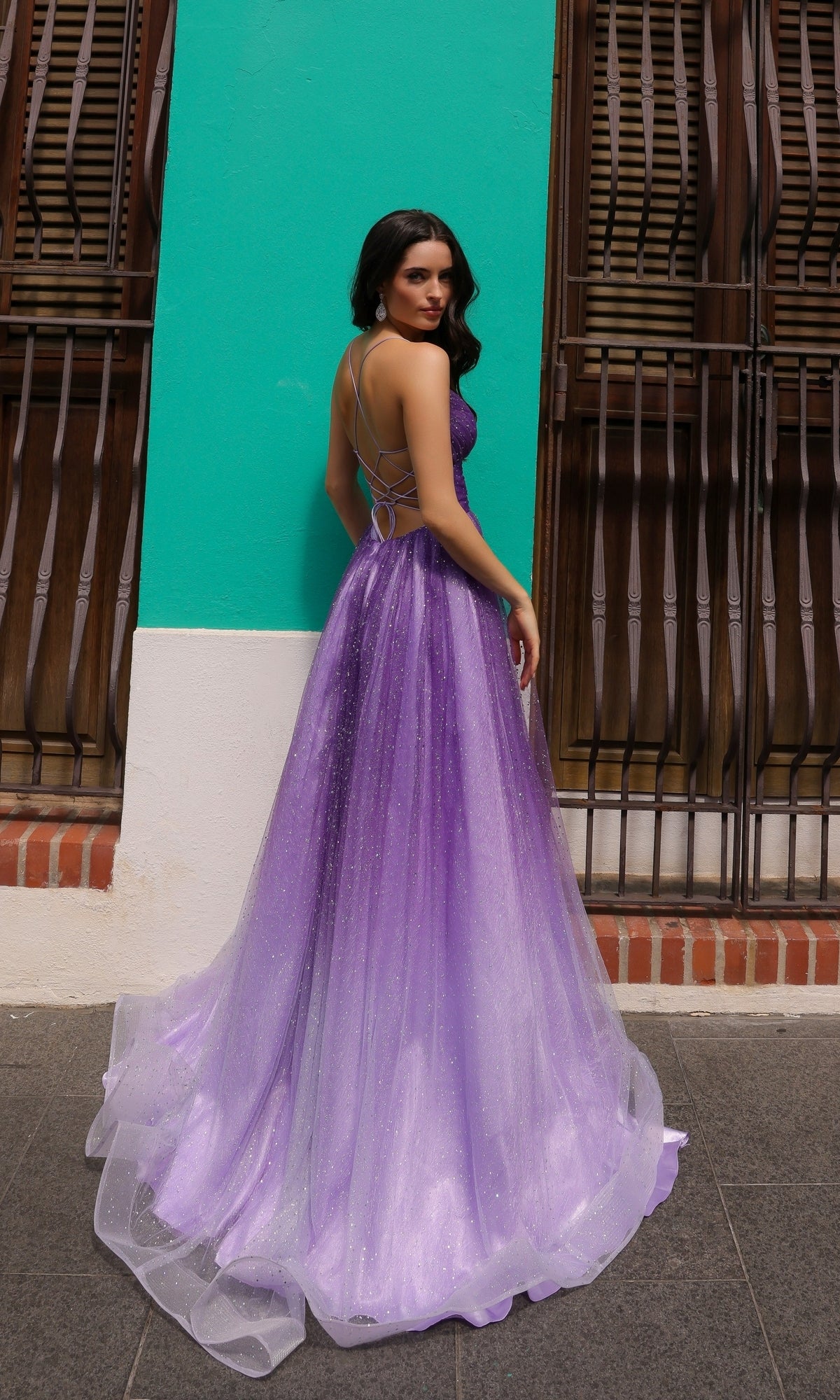 A woman in the Lace-Up Ombre Purple Long A-Line Prom Dress C1251 stands outdoors, facing slightly away, in front of a turquoise wall with wooden windows.