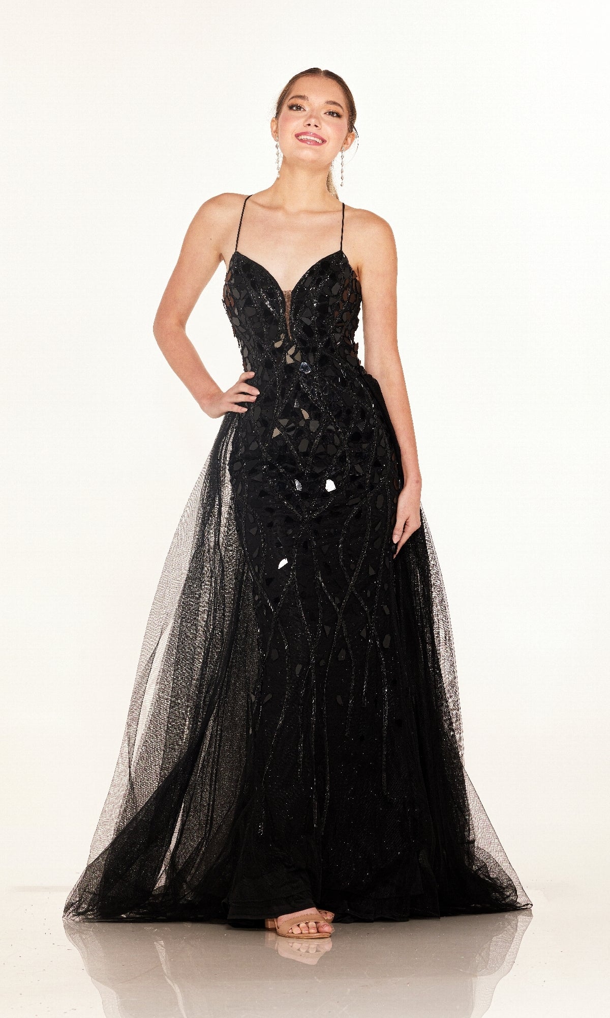 A woman stands against a white background wearing the Cecilia Couture C132, a floor-length black sequin prom dress featuring thin straps and a chic lace-up back.