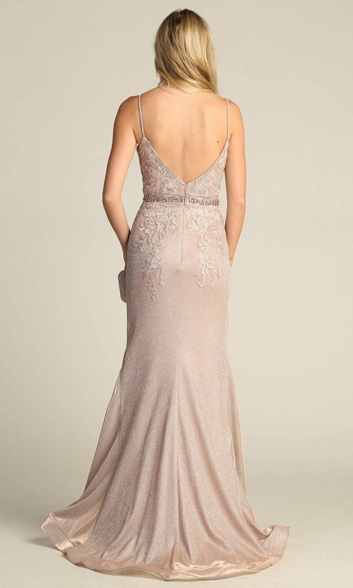 A woman wearing the Low-Back Long Mermaid Prom Dress: Chicas C243, a floor-length light gold gown with spaghetti straps and floral embroidery, stands facing away from the camera.