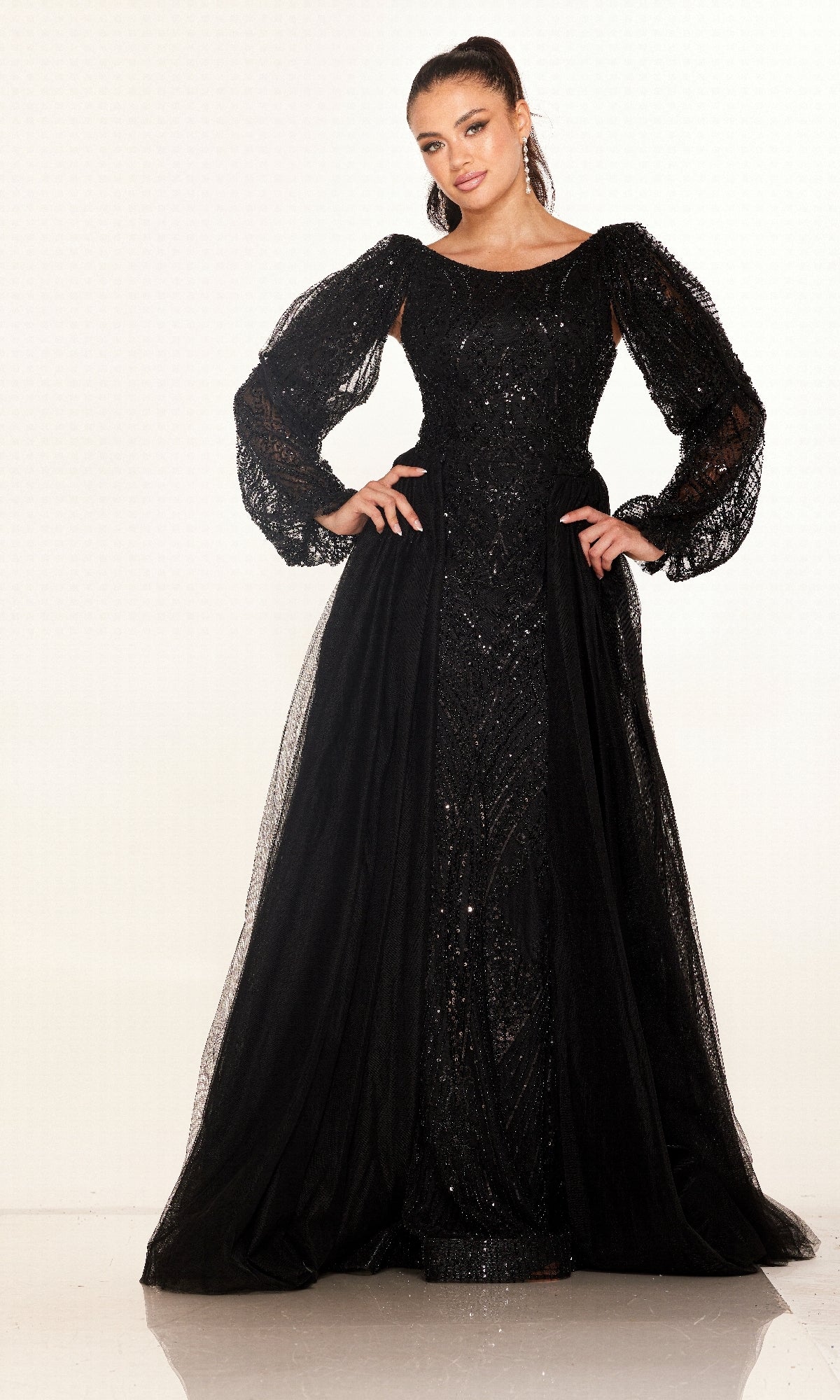 A woman stands with hands on hips, modeling the Cecilia Couture C273 long formal dress featuring black sequin embellishments and sheer puffed sleeves, set against a plain white background.
