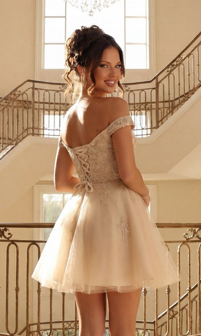 Wearing the Beaded-Corset Short Babydoll Hoco Dress C314, a woman stands on an ornate staircase, smiling and looking over her shoulder in this stylish off-the-shoulder party look.