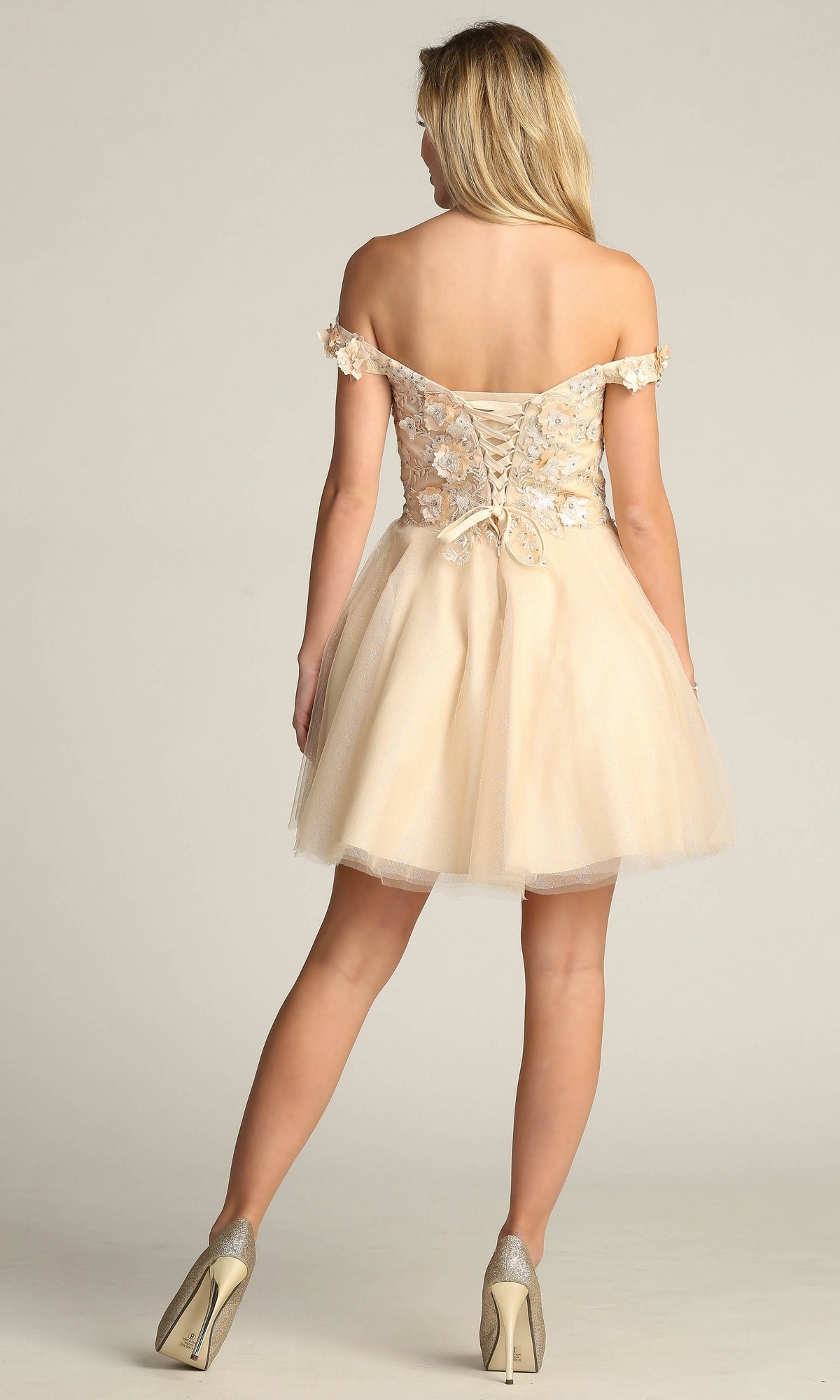 A woman stands facing away, wearing the Beaded-Bodice Short A-Line Homecoming Dress C315, featuring an off-the-shoulder neckline, lace-up back, and tulle babydoll skirt.