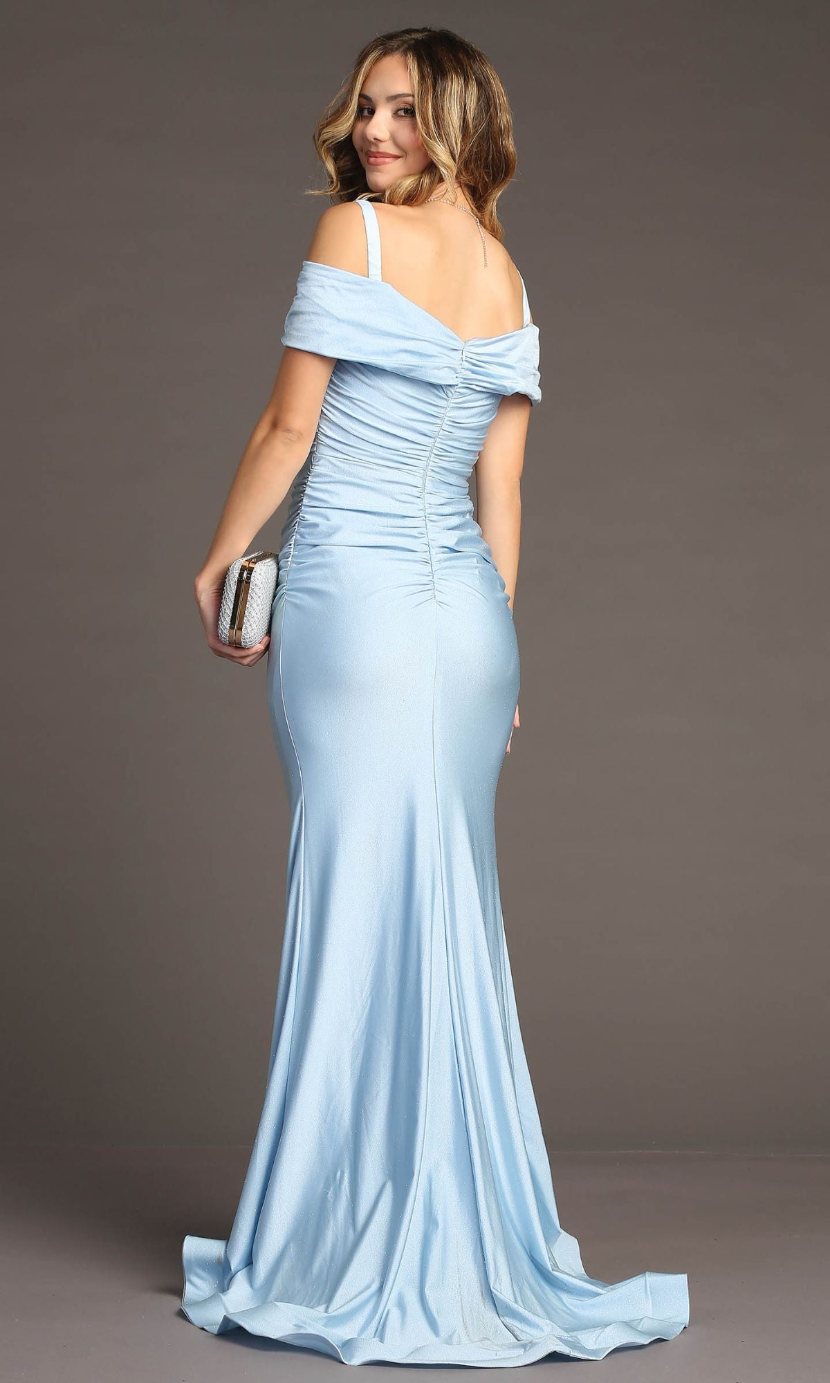 Woman in a Cold-Shoulder Sleek Long Prom Dress: Chicas C325, light blue and off-the-shoulder, holding a silver clutch and standing in a studio, facing away.
