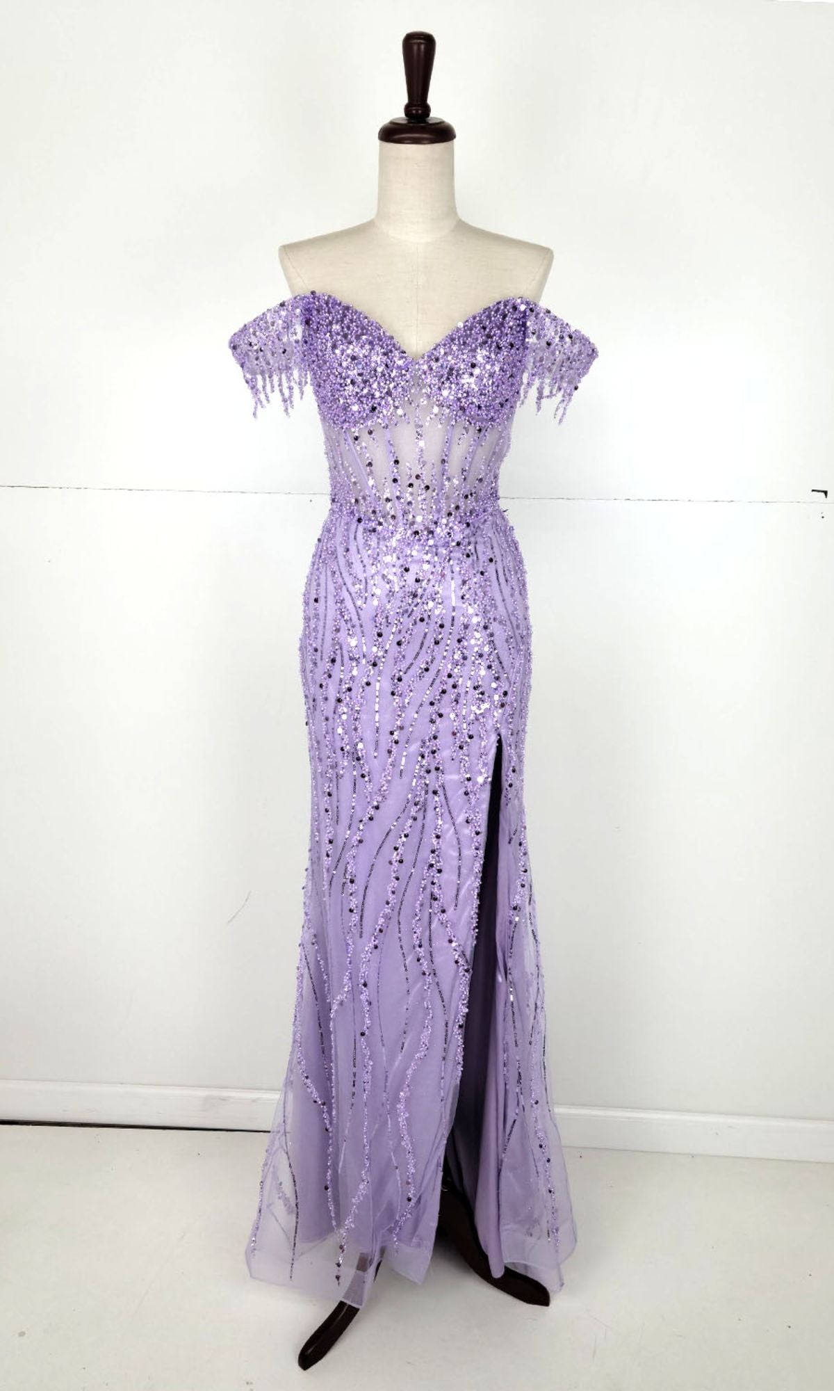 A mannequin showcases the Chicas C331 Off-Shoulder Long Sequin Prom Dress in lavender, featuring a front slit, set against a plain white background.
