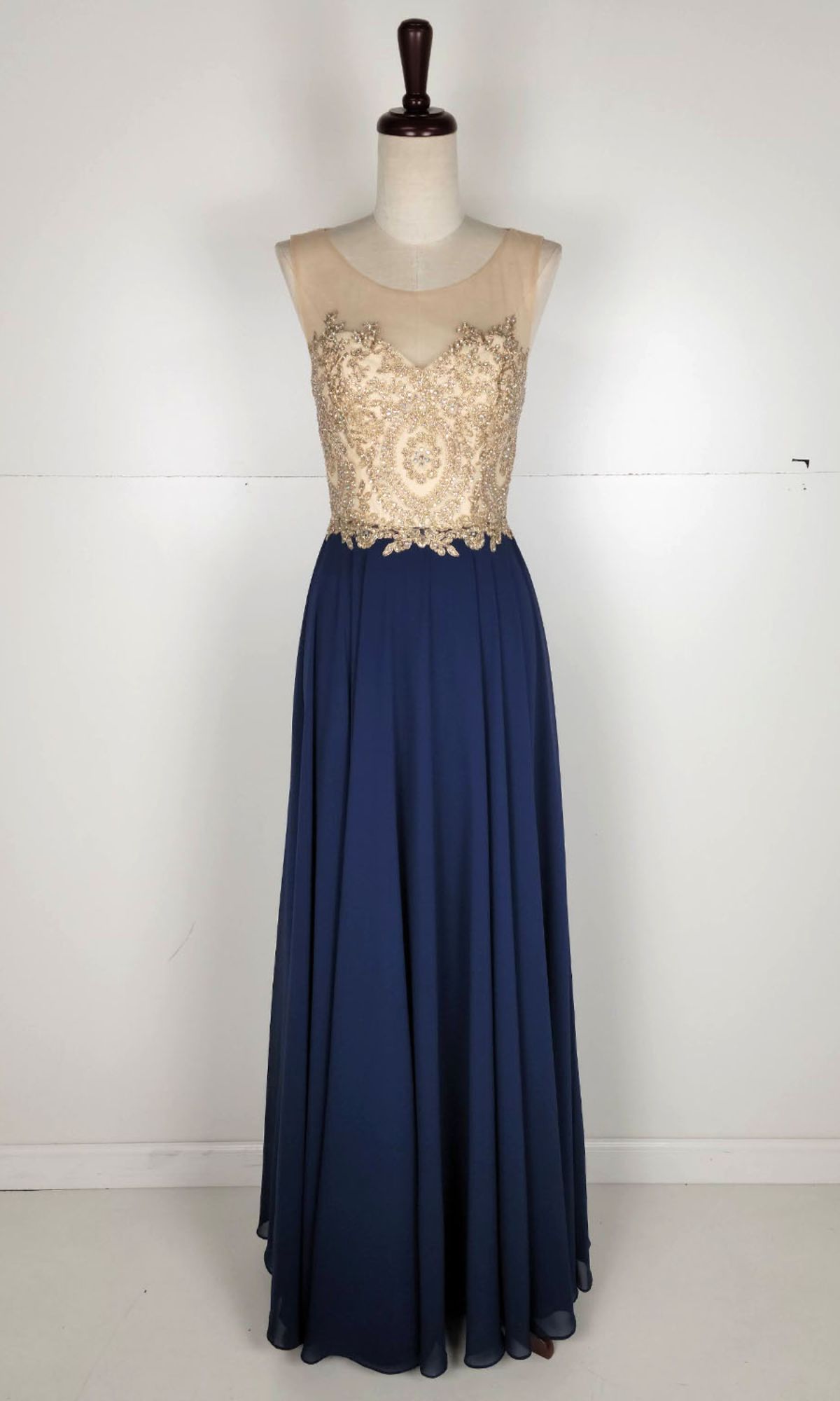 The Embroidered-Bodice Long Prom Dress: Chicas C3320 features a sleeveless sheer beige bodice with gold embroidery and a flowing dark blue A-line skirt, shown on a dress form against a plain background.