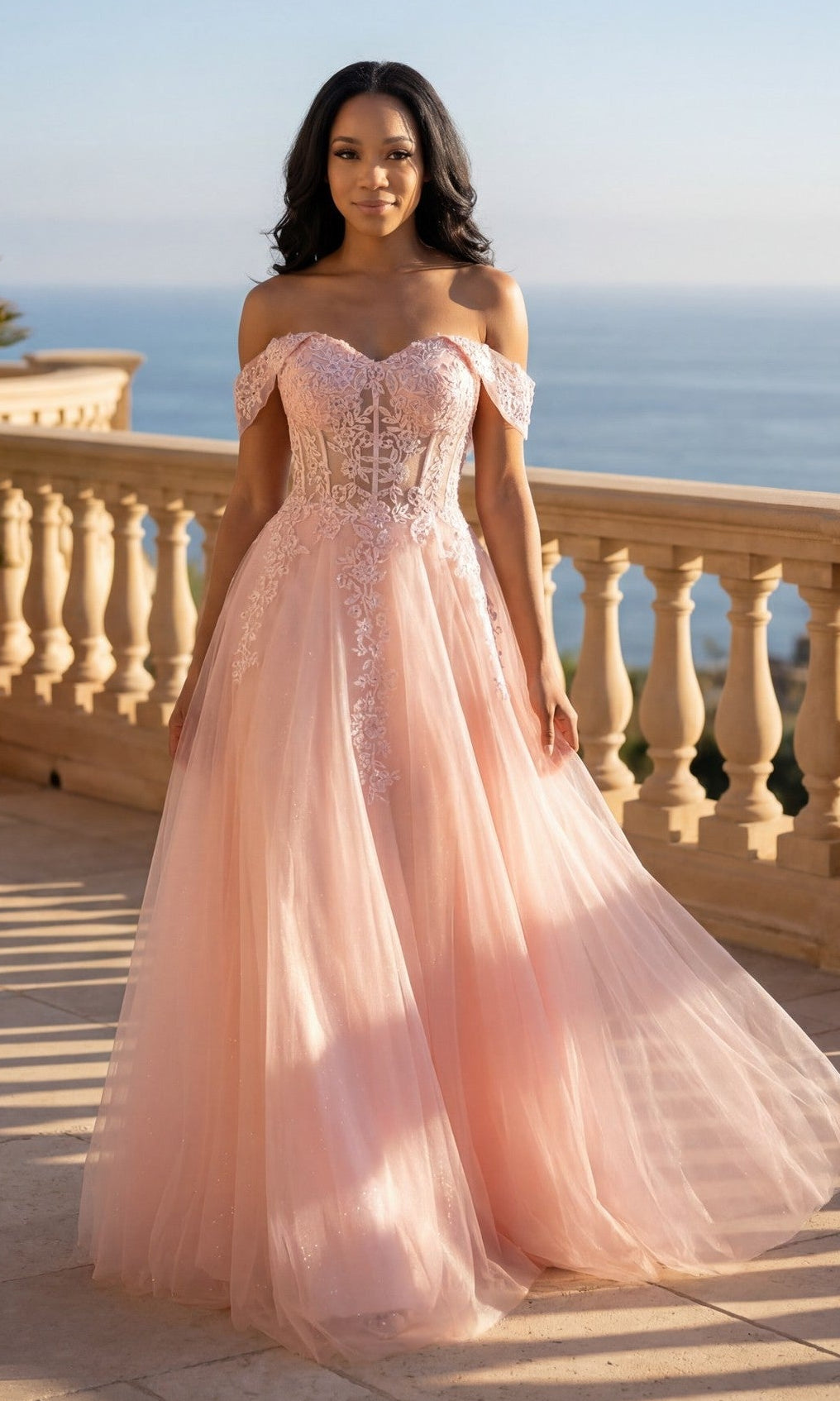 A woman in the blush Long Prom Dress: Chicas C336 stands on a sunlit balcony with a scenic ocean view in the background.
