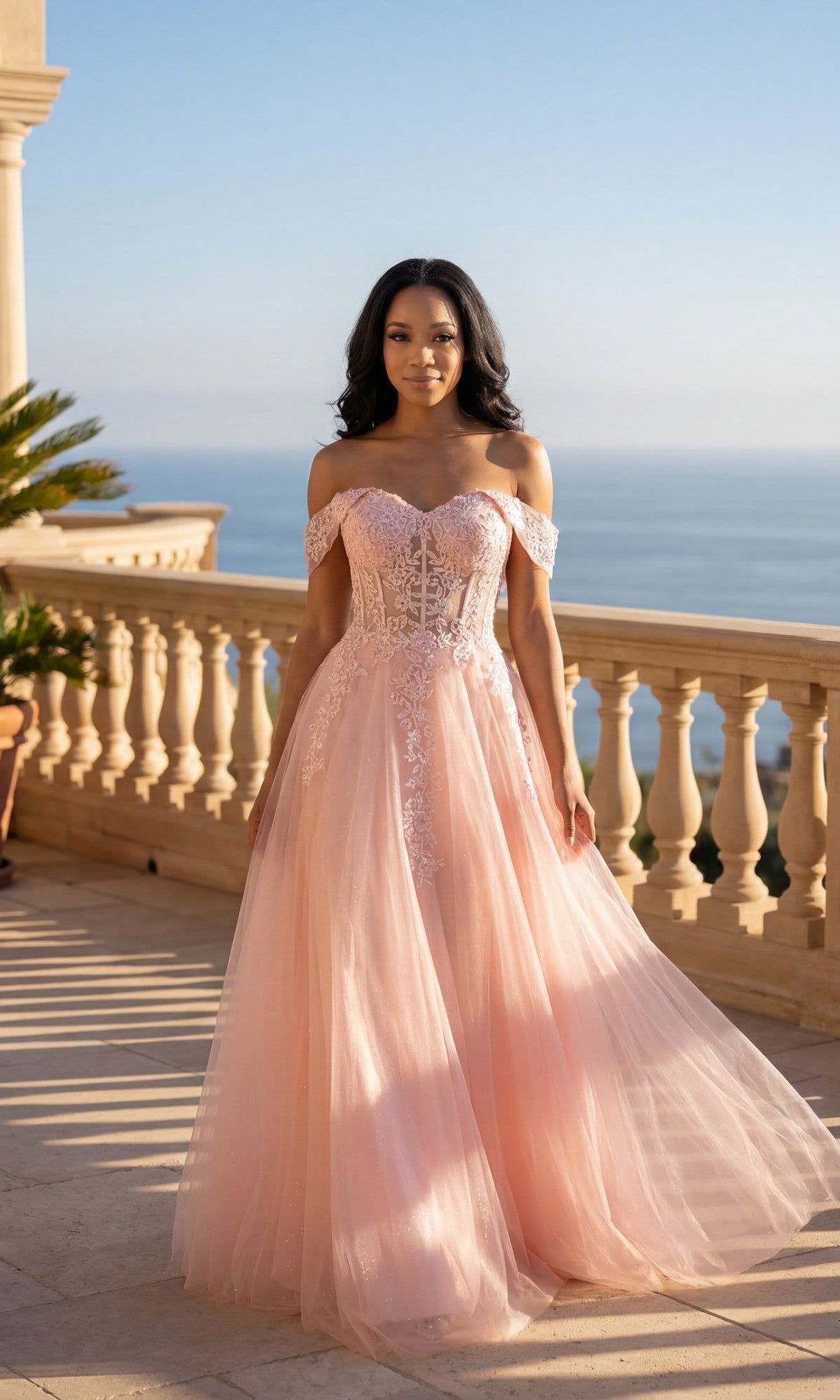 A woman in the blush Long Prom Dress: Chicas C336 stands on a sunlit balcony with a scenic ocean view in the background.