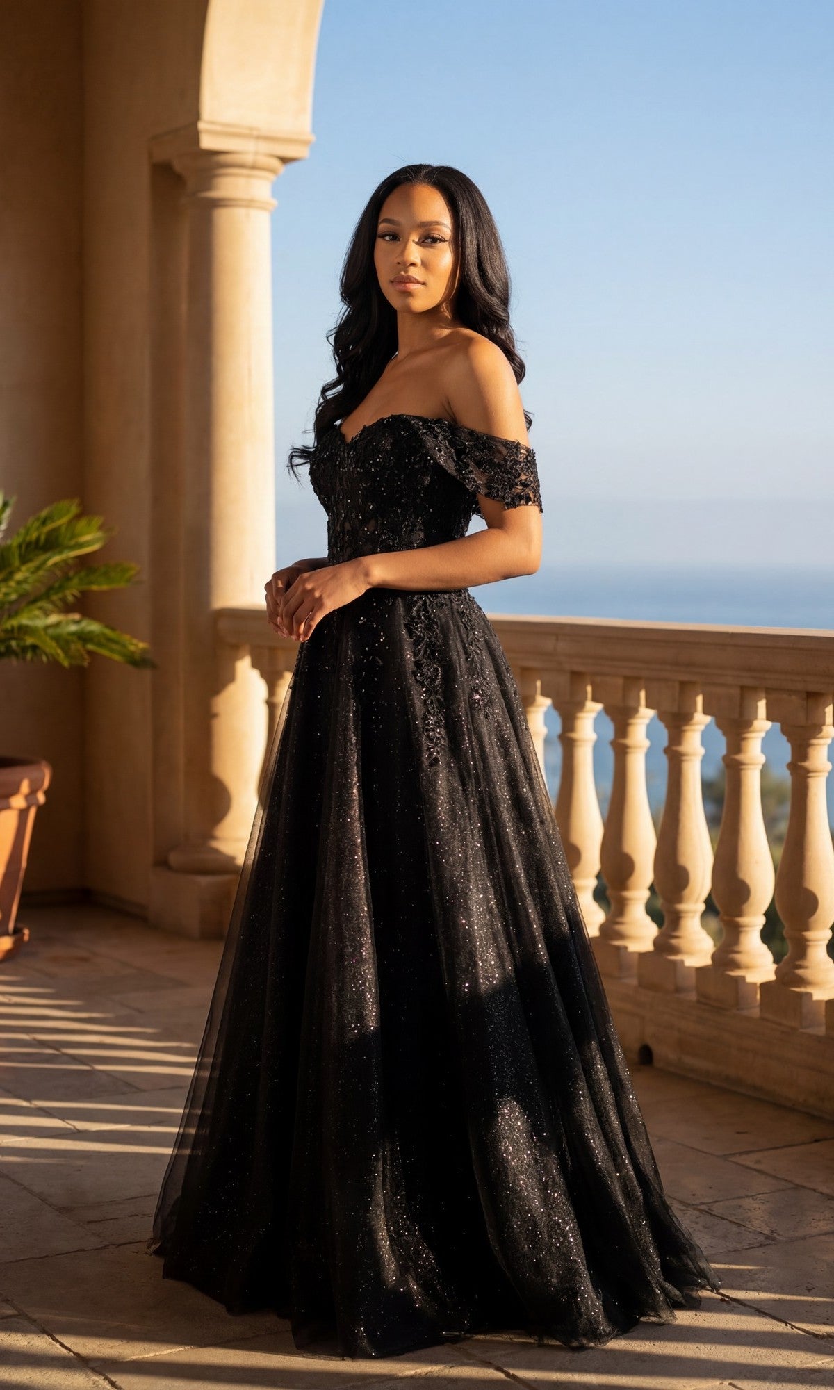 A woman in the black Long Prom Dress: Chicas C336 with off-the-shoulder floral lace embroidery stands on a columned balcony overlooking the ocean and sky.