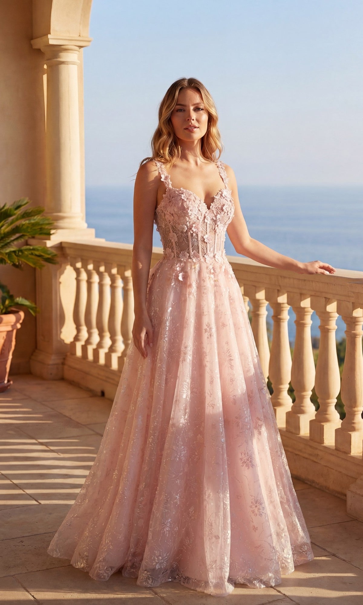 A woman in a blush Long Prom Dress: Chicas C370 with floral lace embroidery stands on a sunlit balcony, the ocean glistening in the background.
