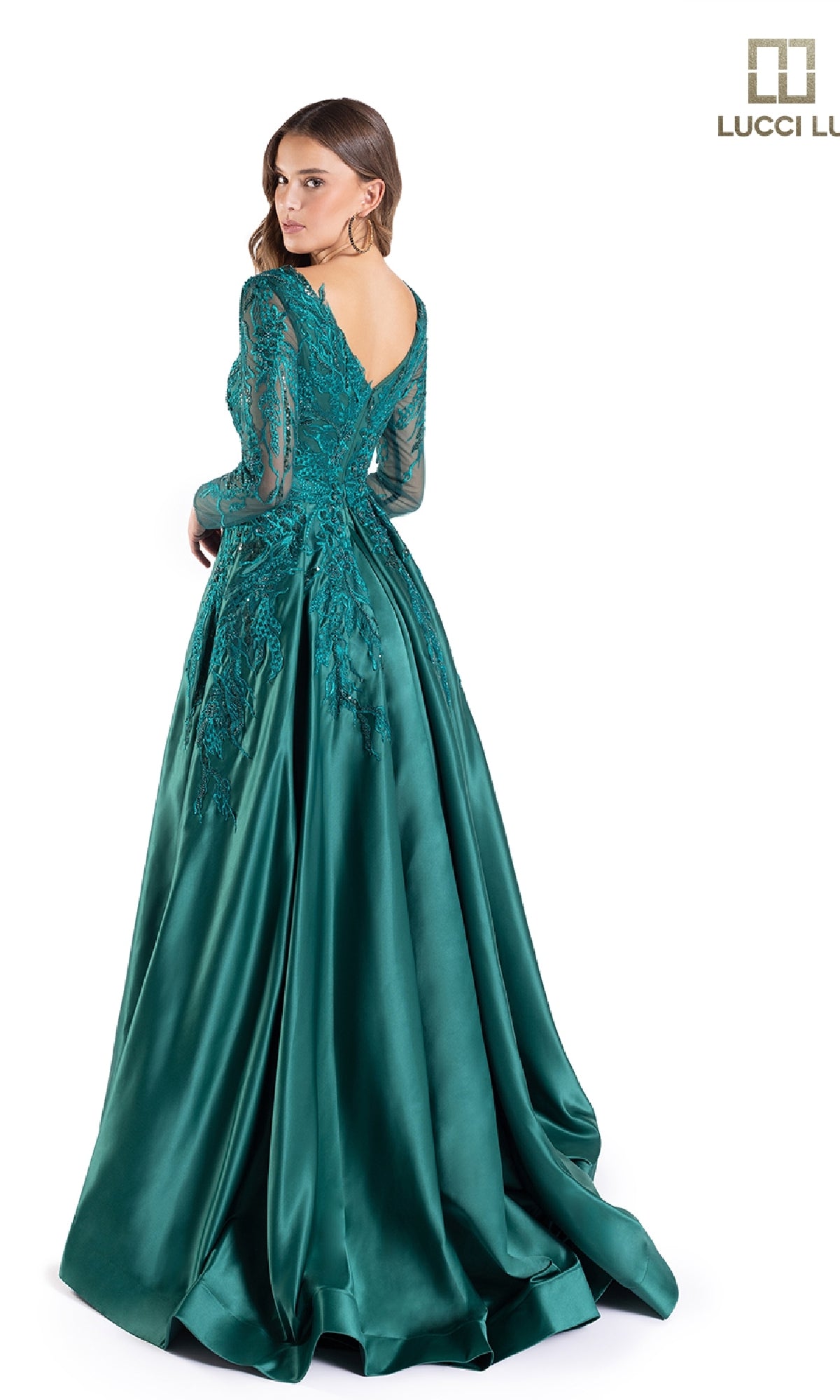 A woman stands gracefully, looking over her shoulder in the Lucci Lu C8045 long formal dress, featuring emerald green fabric, lace sleeves, sparkly embroidery, and a V-shaped back.